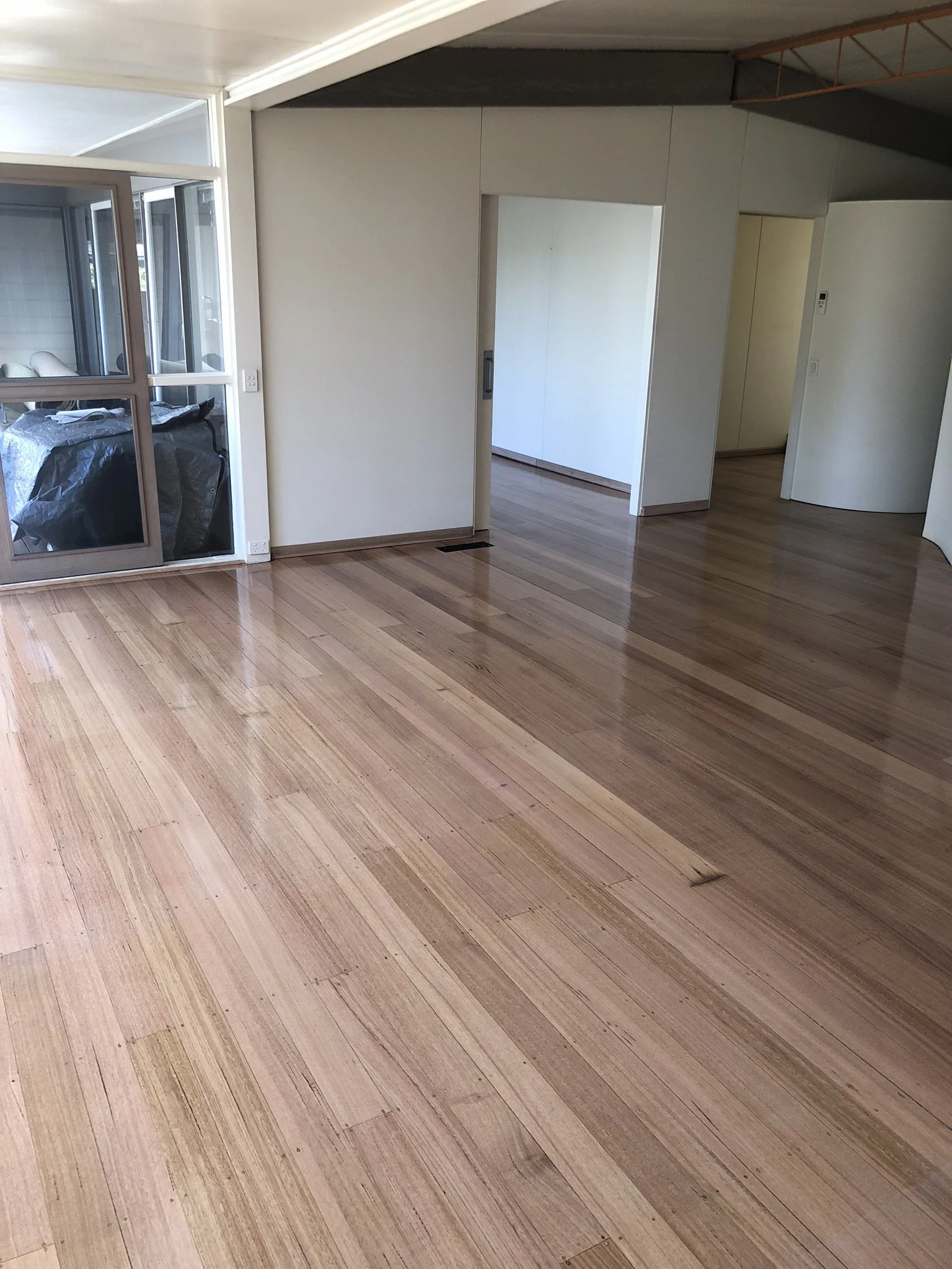 Empty room with polished wooden floors and white walls, some chrome accents, and a sliding glass door leading to a small enclosed porch with visible outdoor furniture.
