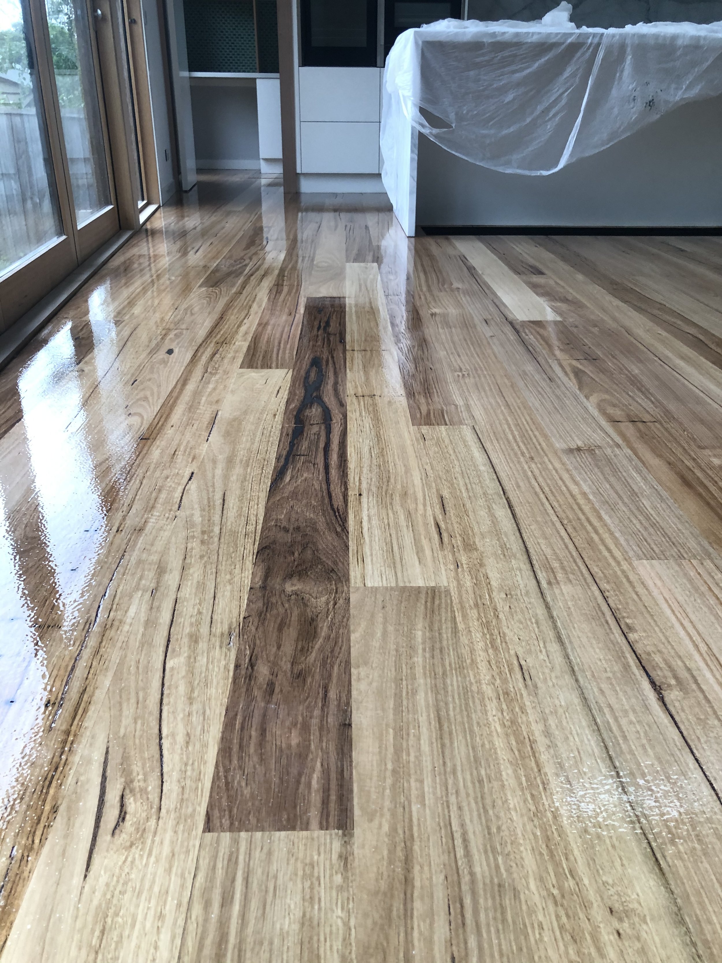 Recently cleaned and polished wooden floor in a modern kitchen with glass sliding doors and natural light.