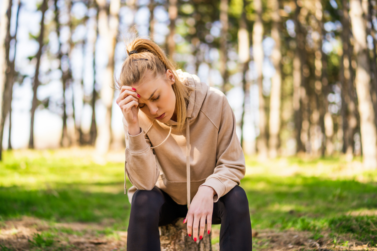 femme fatiguée assise en forêt tenant sa tête exprimant une fatigue chronique