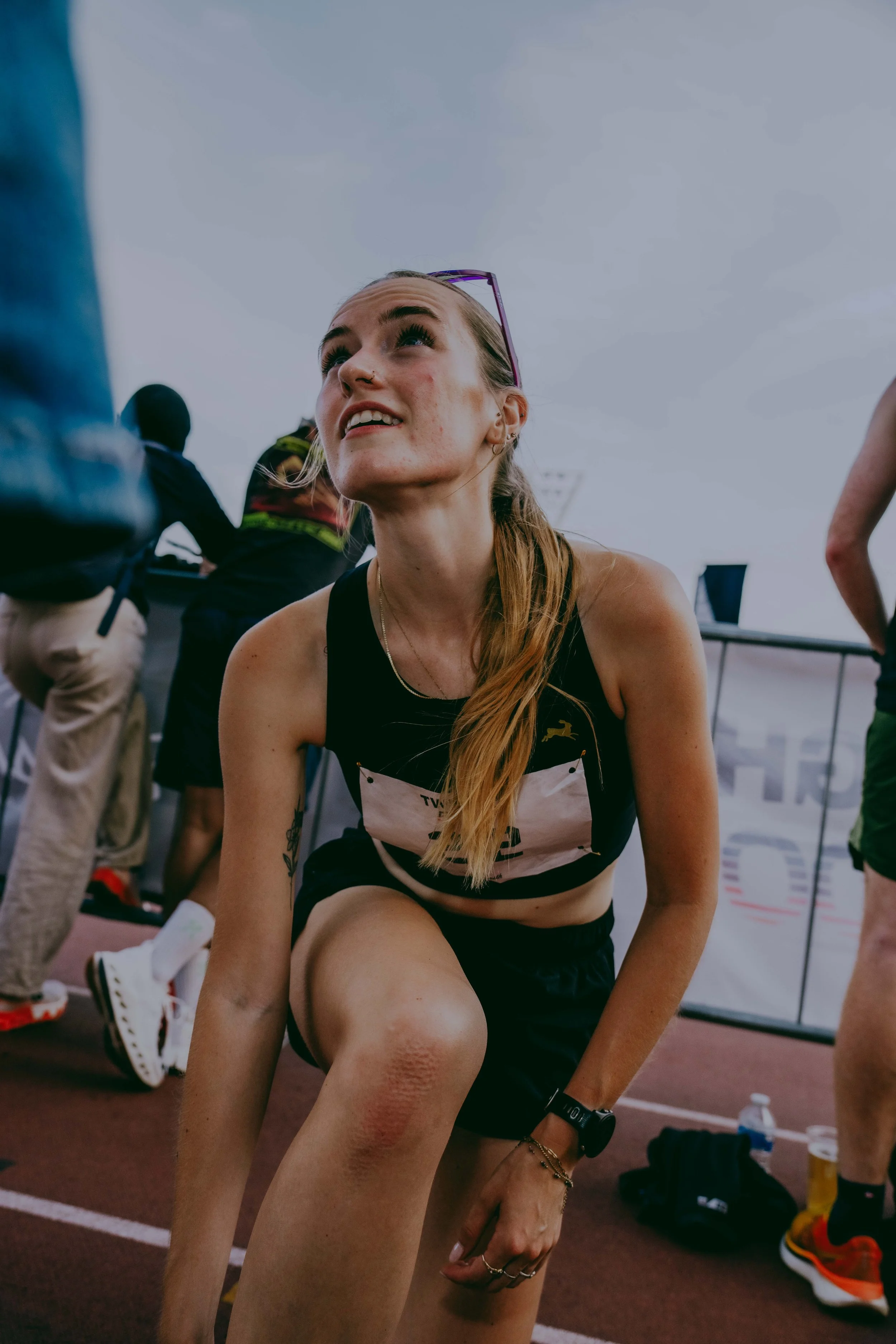 Young woman in sportswear stretching on a track field at an athletics event.