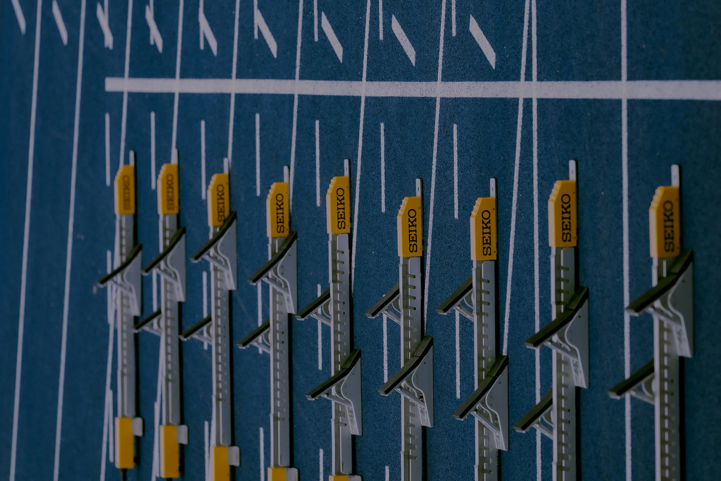 Close-up of multiple yellow and black sewing machine parts labeled 'SEIKO' mounted on a blue surface with white grid lines.