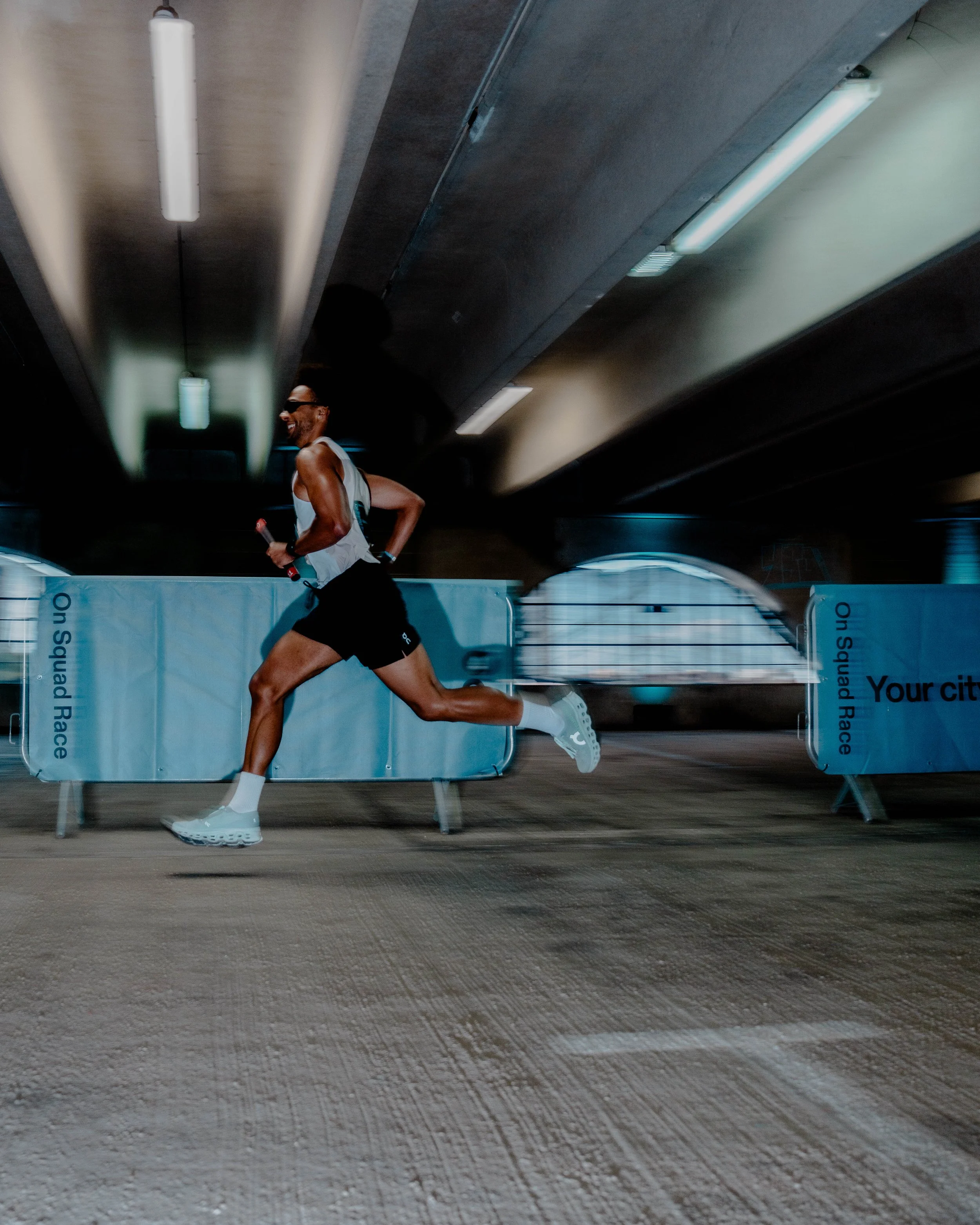 A man running in an indoor sports area, possibly a gym or fitness center, with fluorescent lighting and a curved barrier or wall in the background.