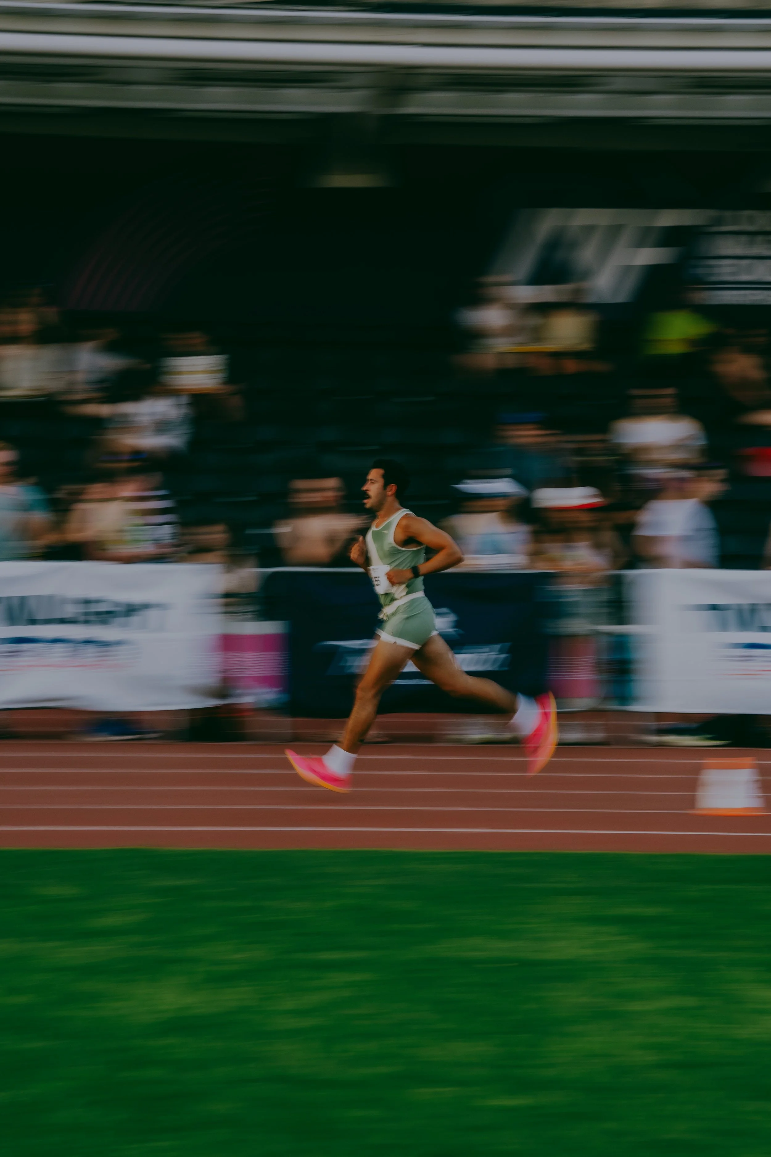 A male athlete running on a track in a stadium during a race, with motion blur indicating speed.
