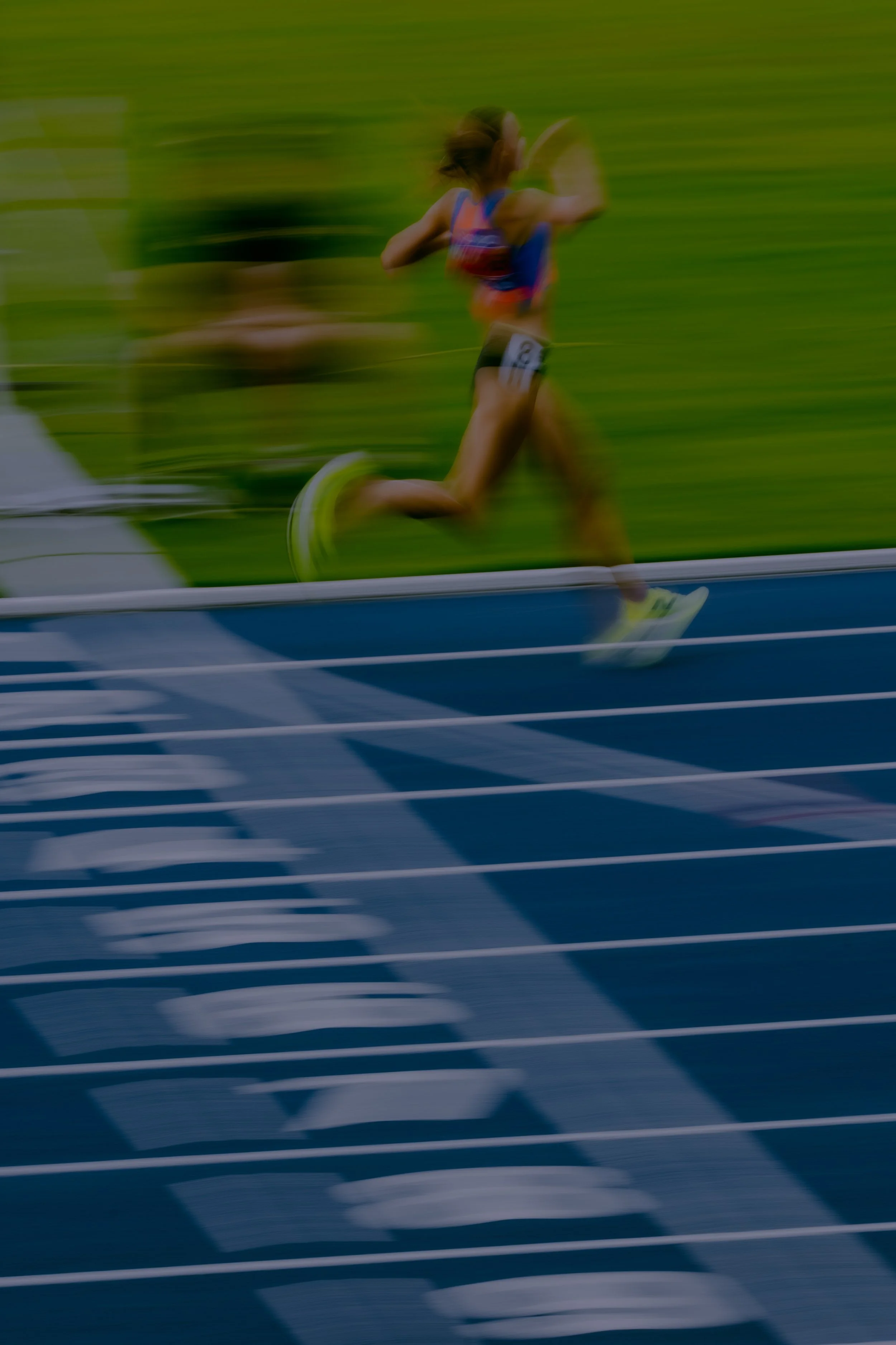 A female athlete running on a track with a grassy field in the background, captured with motion blur.