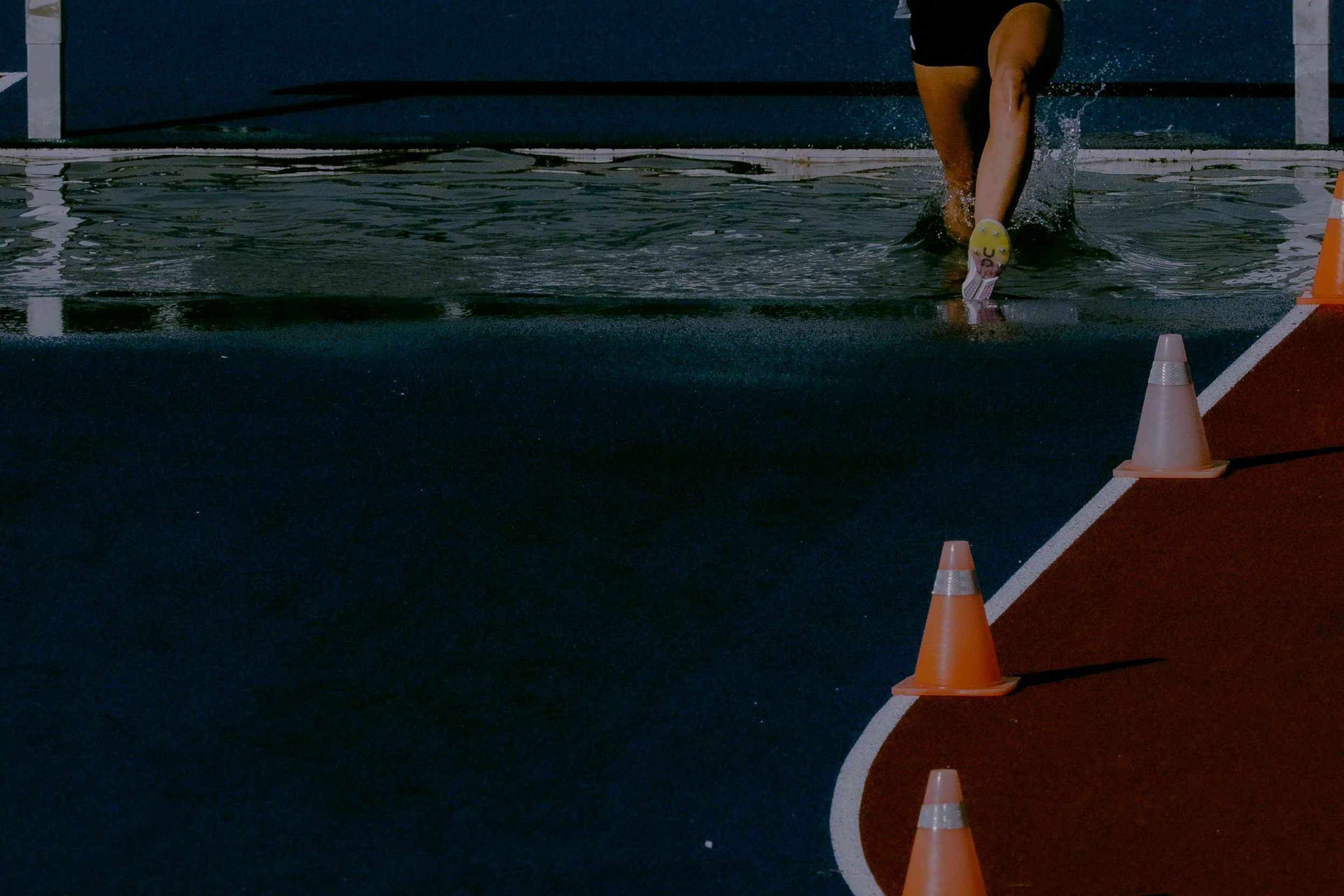 Person running on a track during a race, wearing running shoes, with orange cones placed along the track.