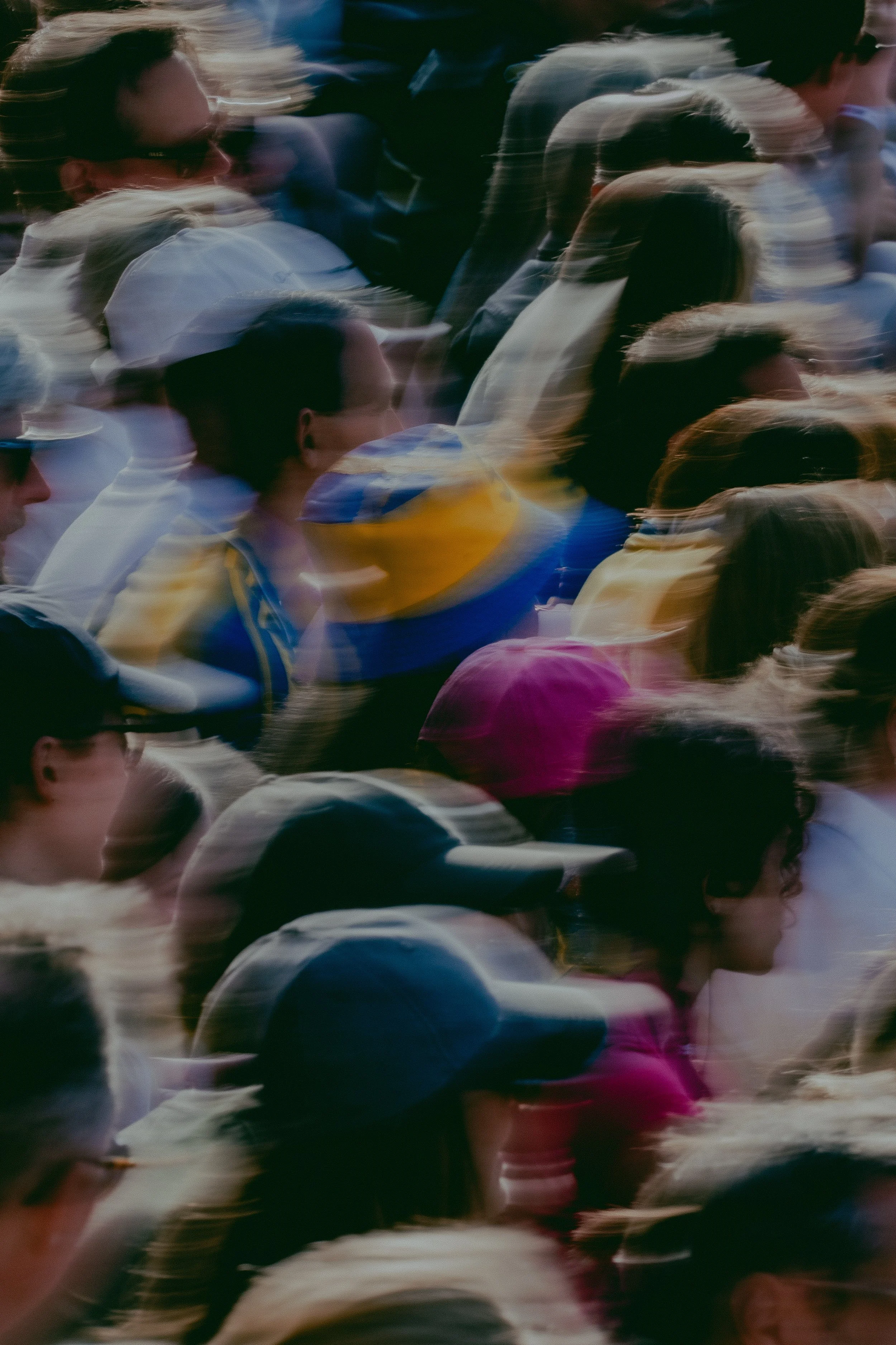 Blurred photo of a crowd of people walking outside, with many wearing white or light-colored clothing and some wearing hats or sunglasses.