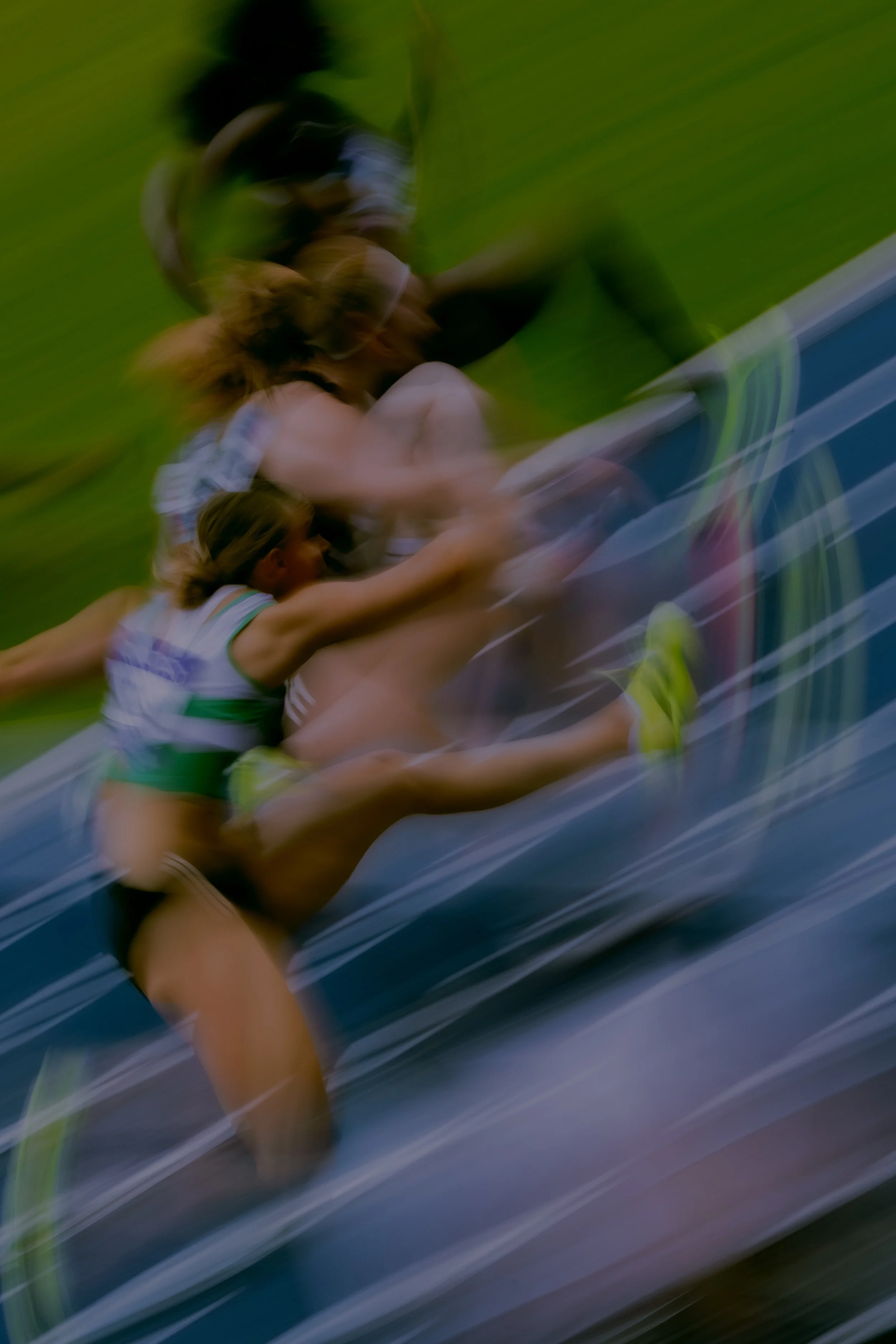 Two female athletes are in a sprint race, running on an outdoor track with a grassy around. motion blur indicates high speed.
