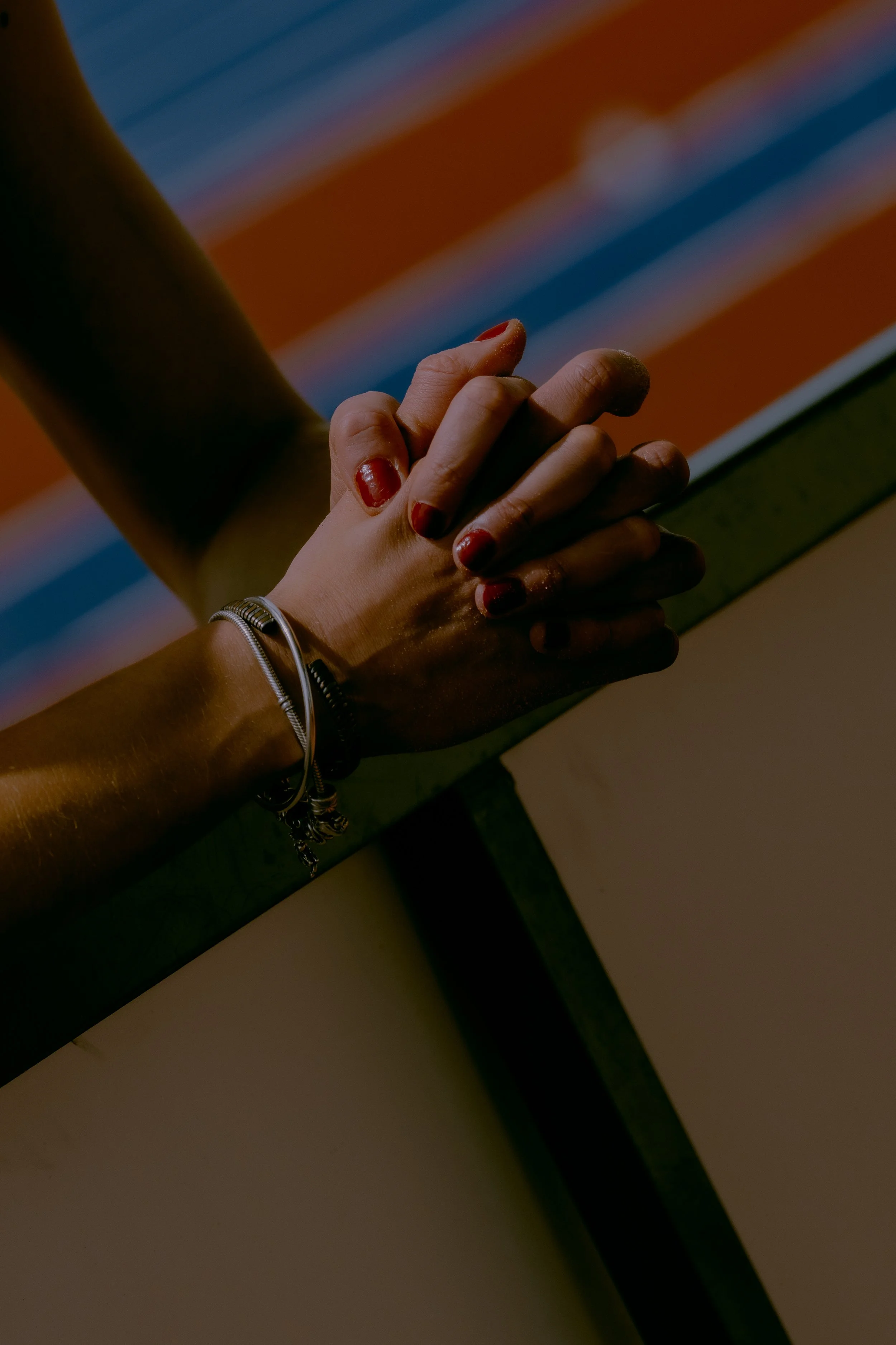Close-up of two hands clasped together, one with painted nails, in front of a colorful striped background.