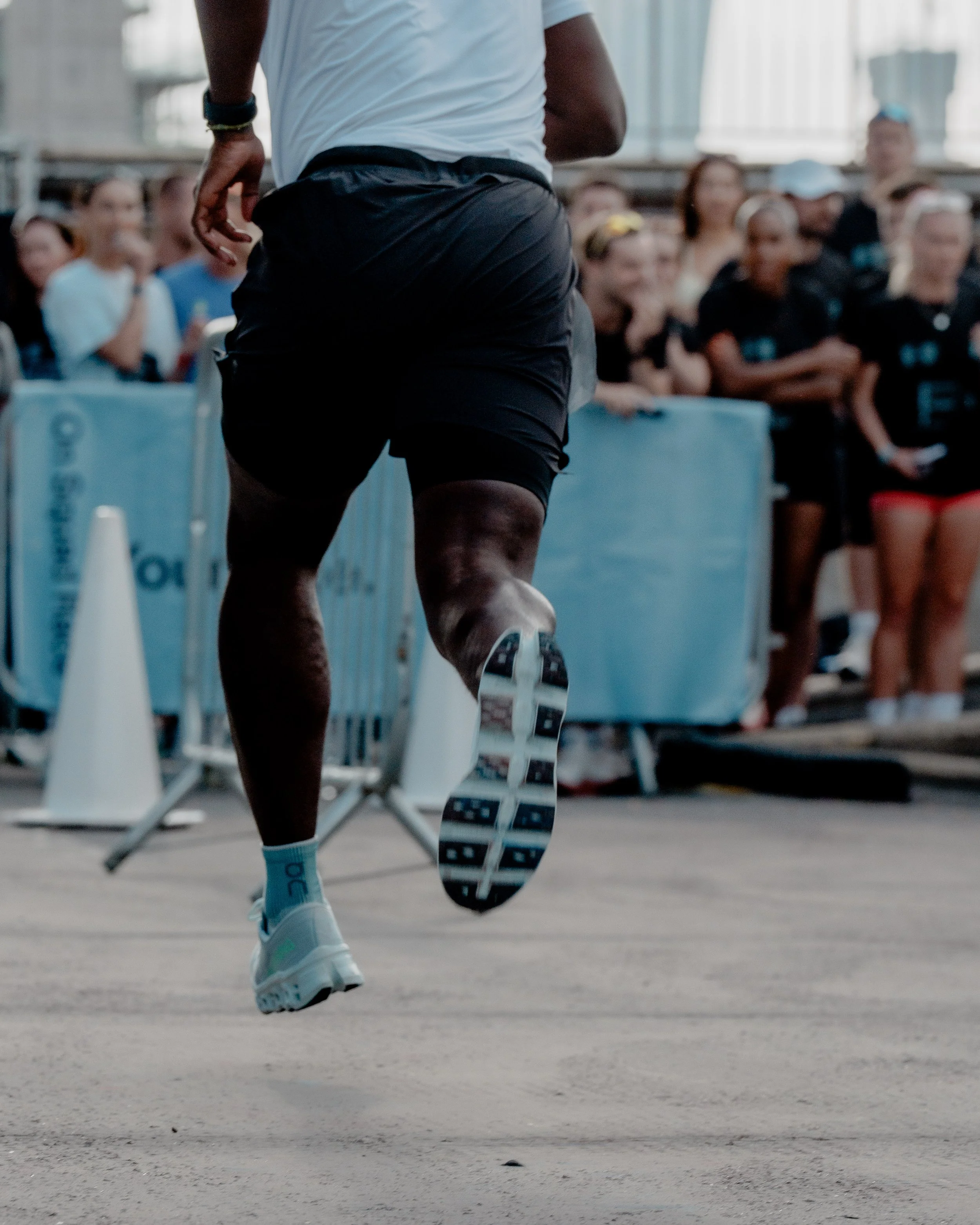 A person running outdoors at a race event, wearing a white shirt, black shorts, and running shoes.
