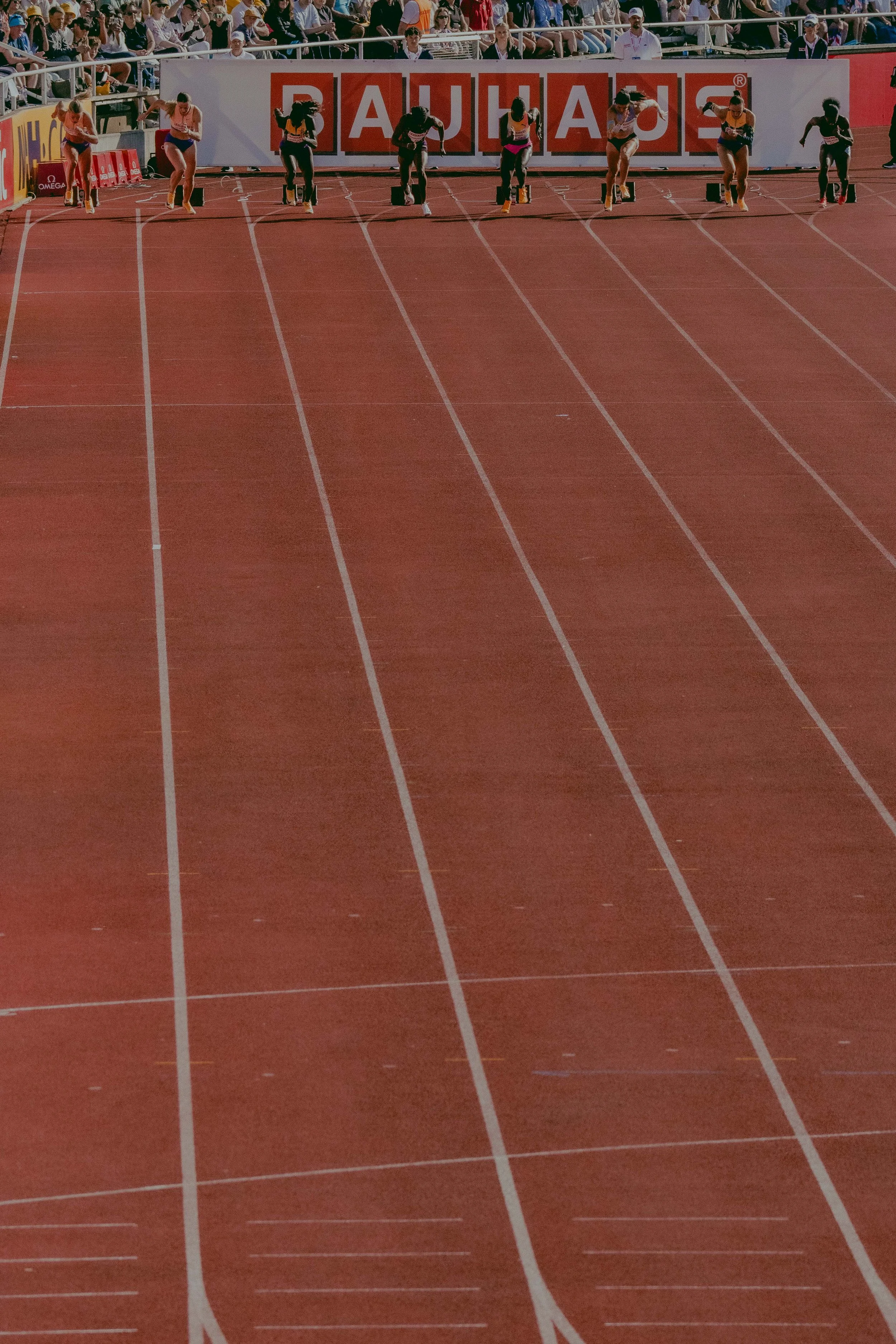 Track and field athletes at the starting blocks ready for a race with a crowd in the stands.