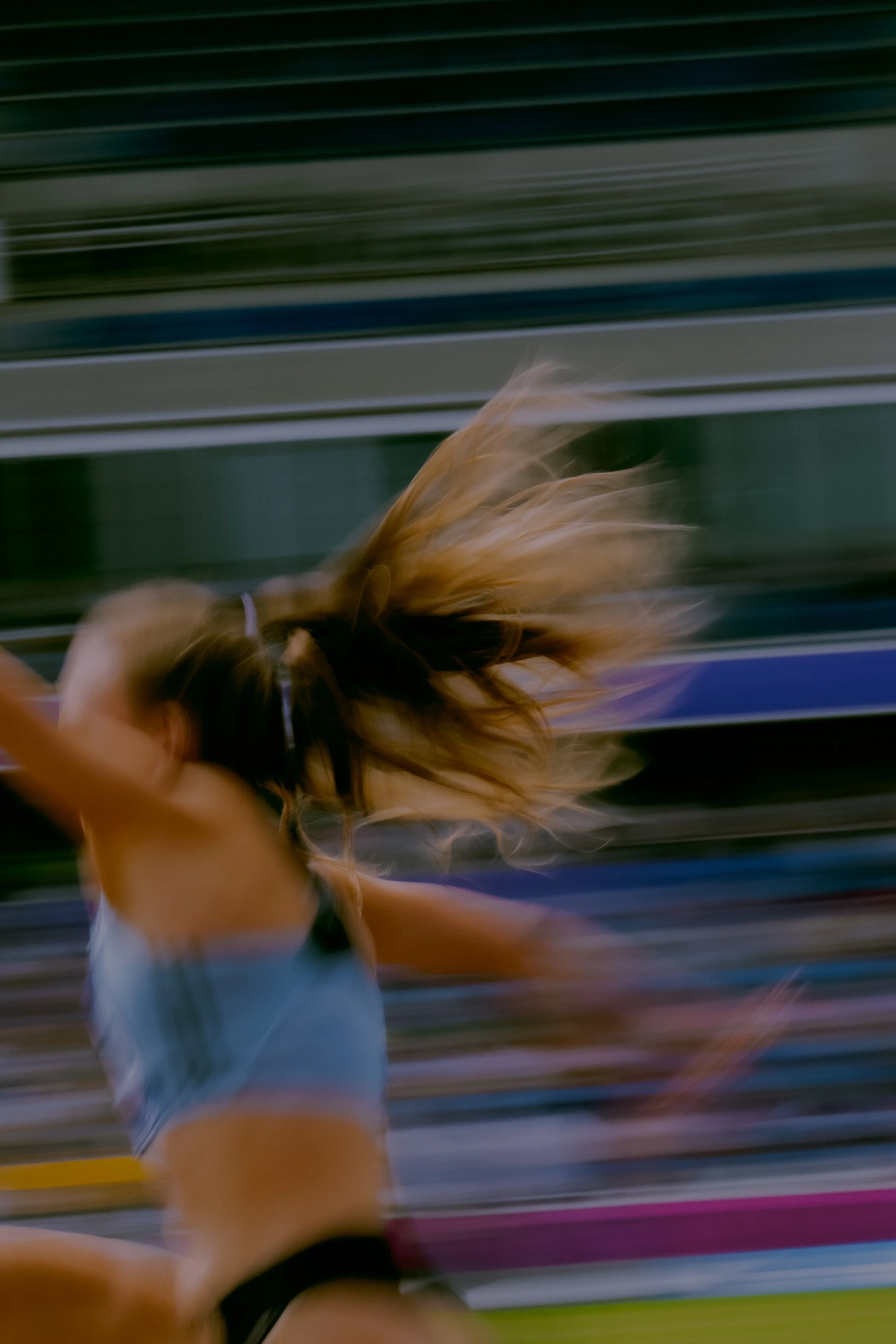 A blurred photo of a woman with long hair running on a track. The background features horizontal lines in green, gray, blue, purple, and yellow.