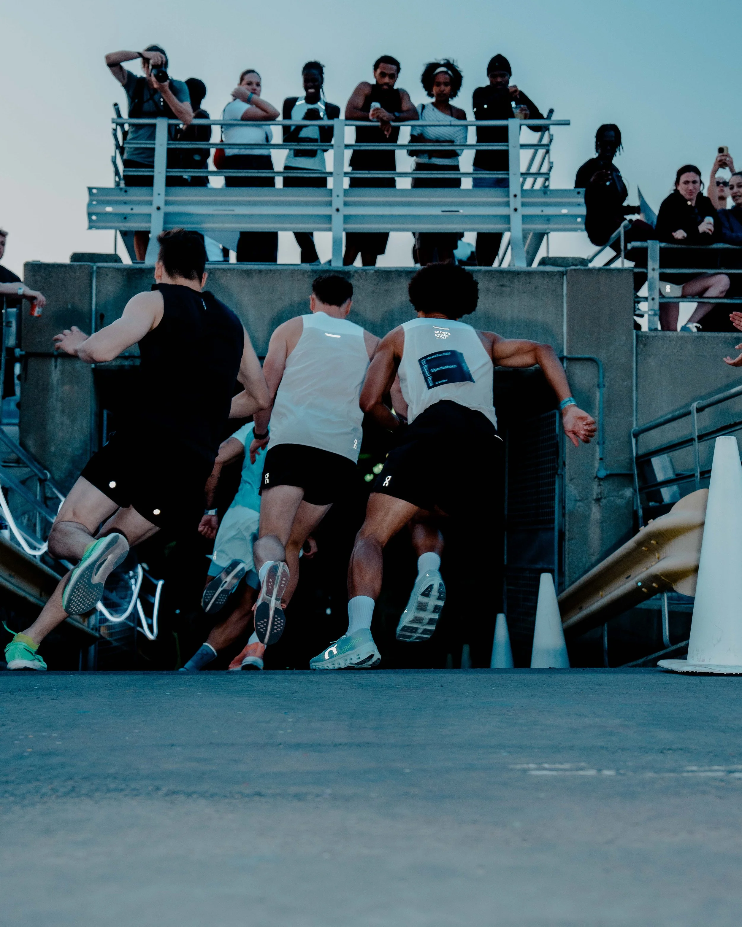 Runners participating in a race, with some exiting the starting position, and spectators watching from an elevated platform.