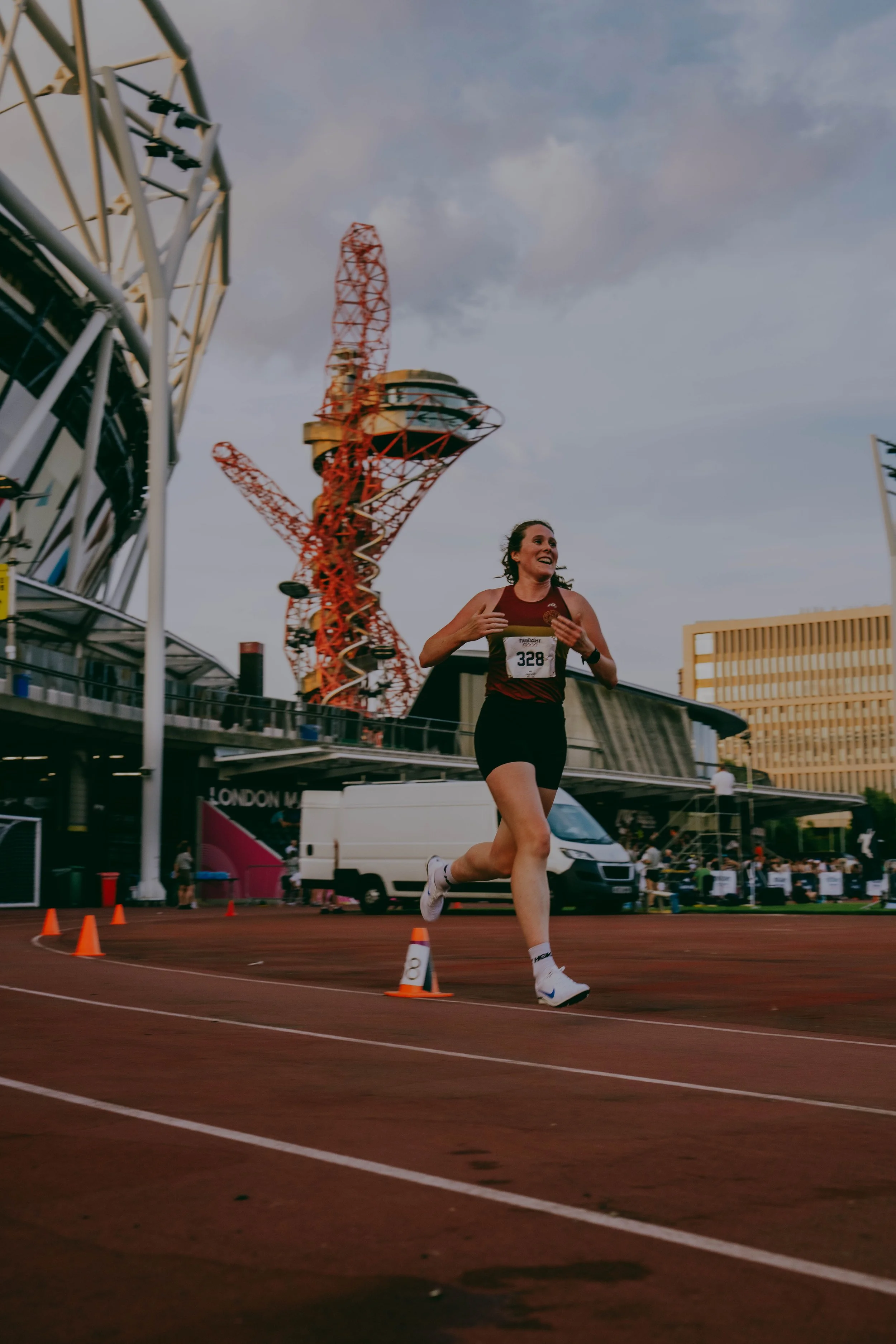 Female runner on a track field, with amusement park rides and buildings in the background, during daytime.