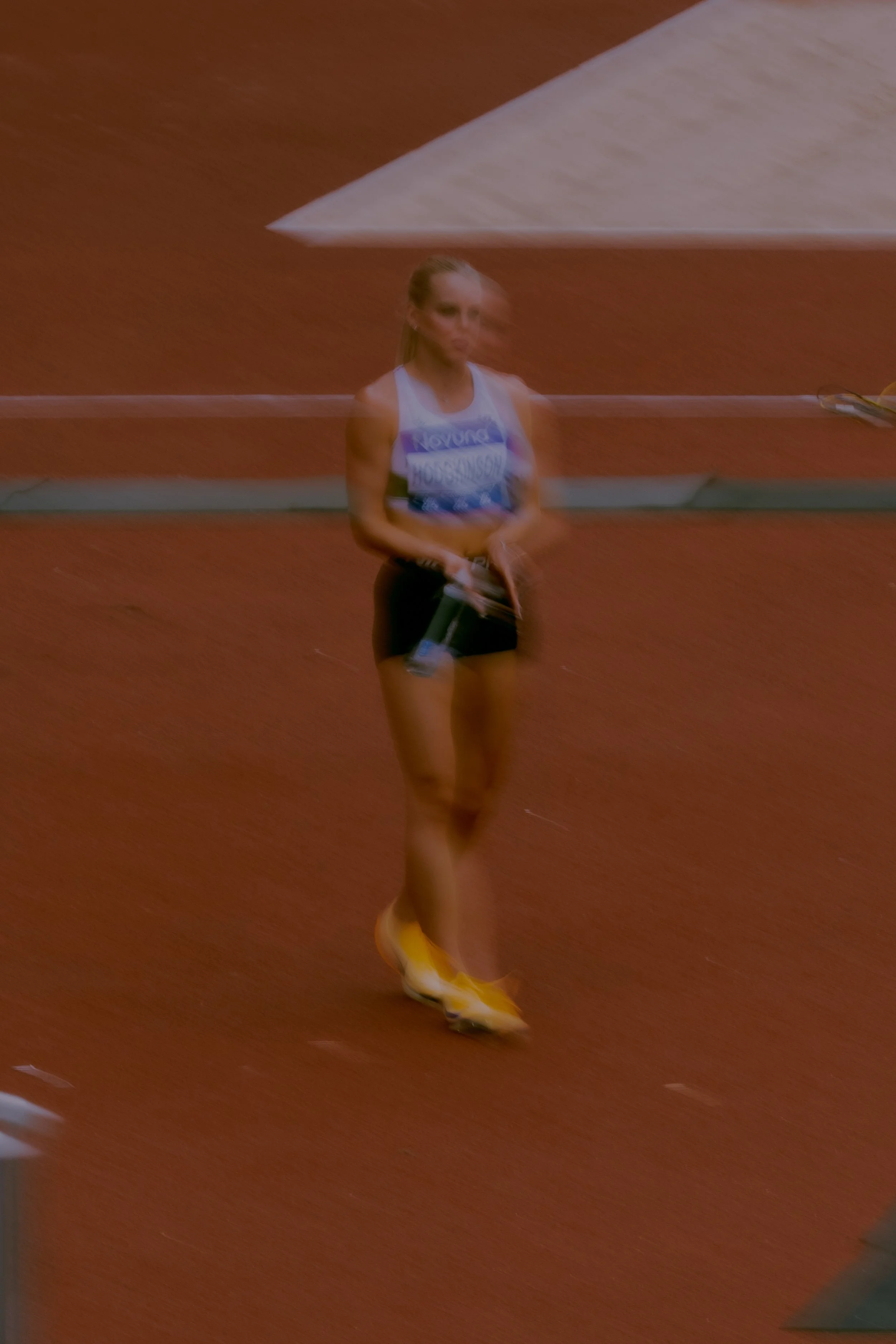 A woman running on a red track in athletic attire with a bib number, near the finish line.
