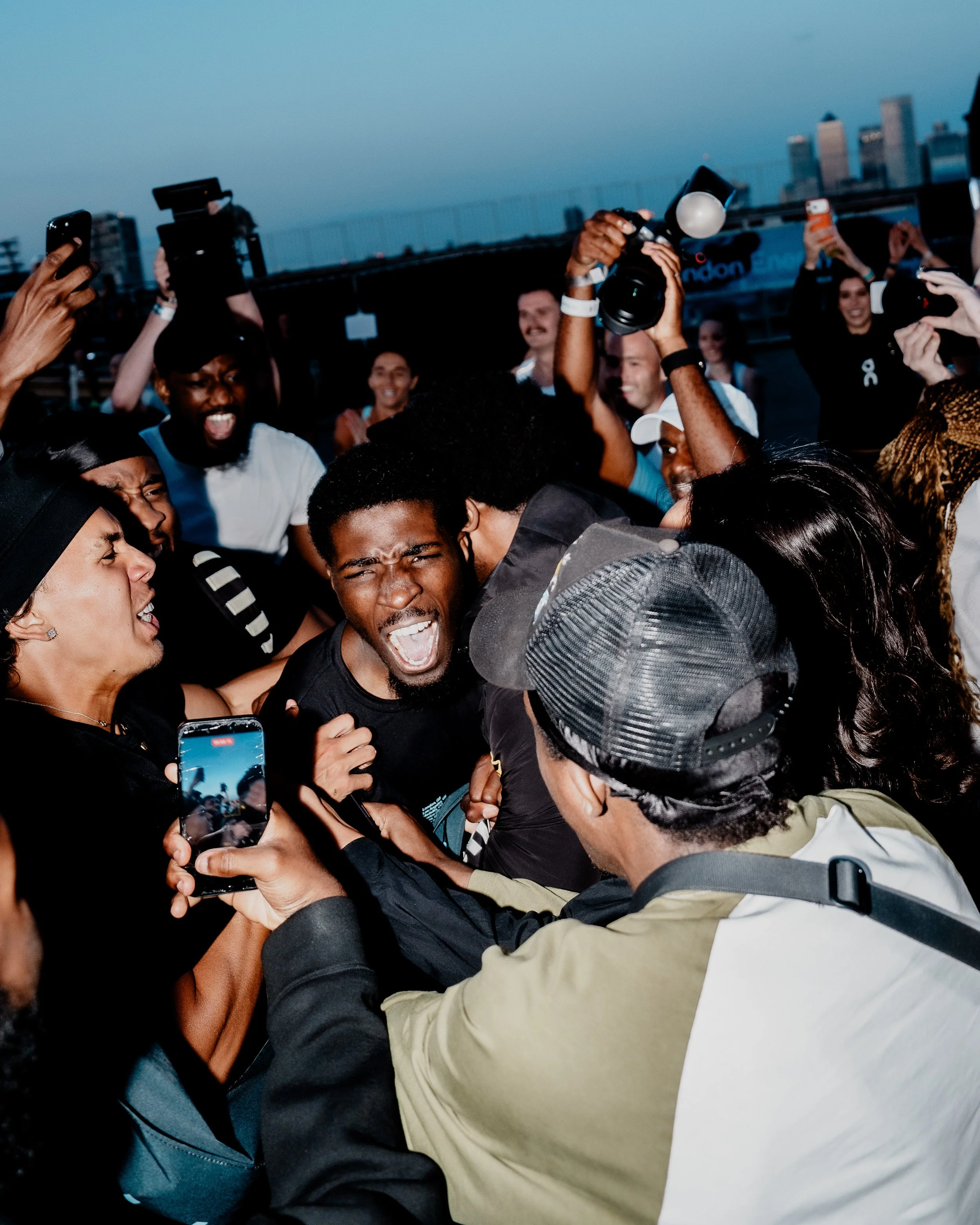 Group of people taking selfies and videos, some smiling and cheering, during a social event or celebration outdoors in the evening.