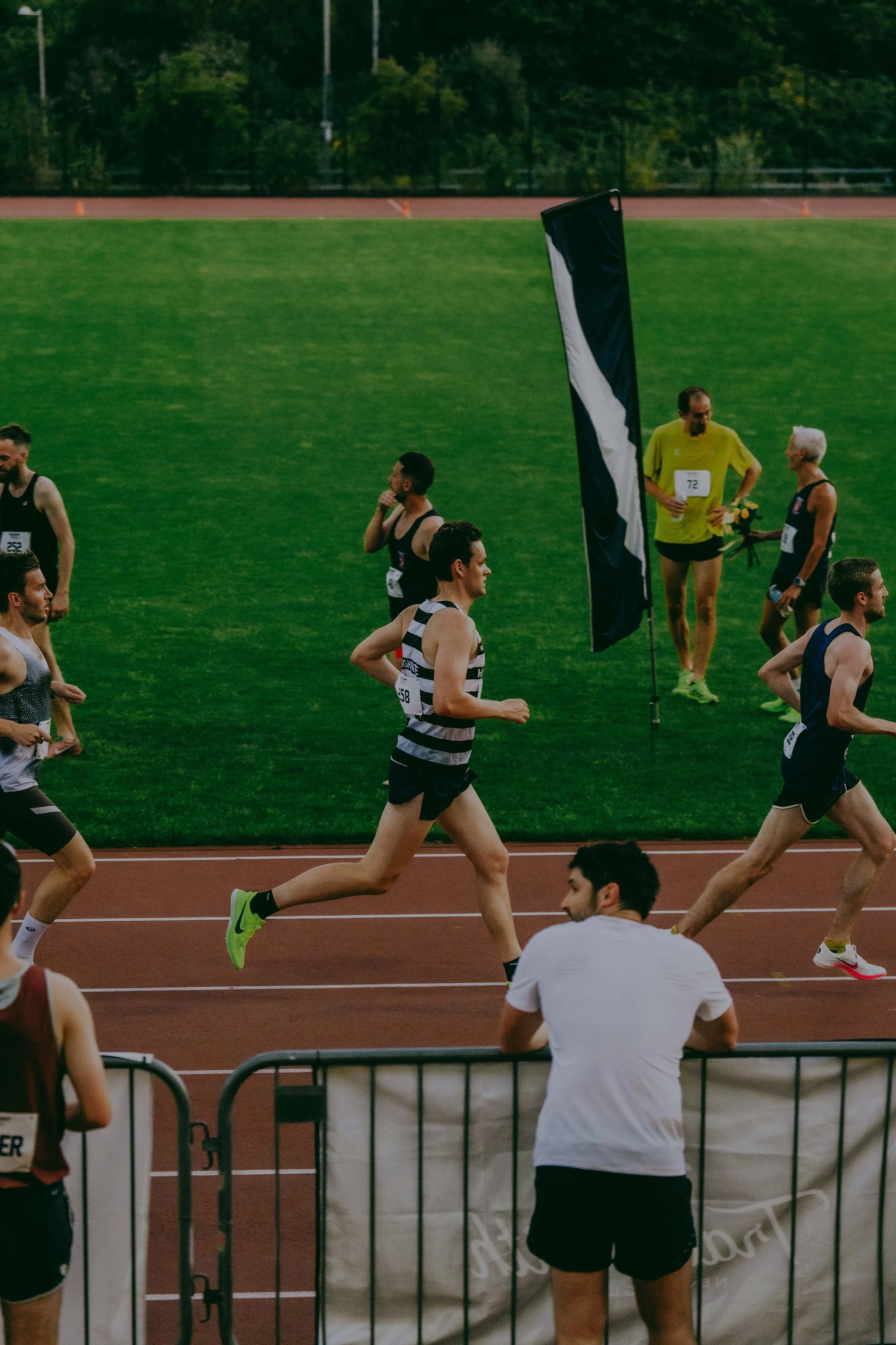 People running on a track with a grassy field and trees in the background.