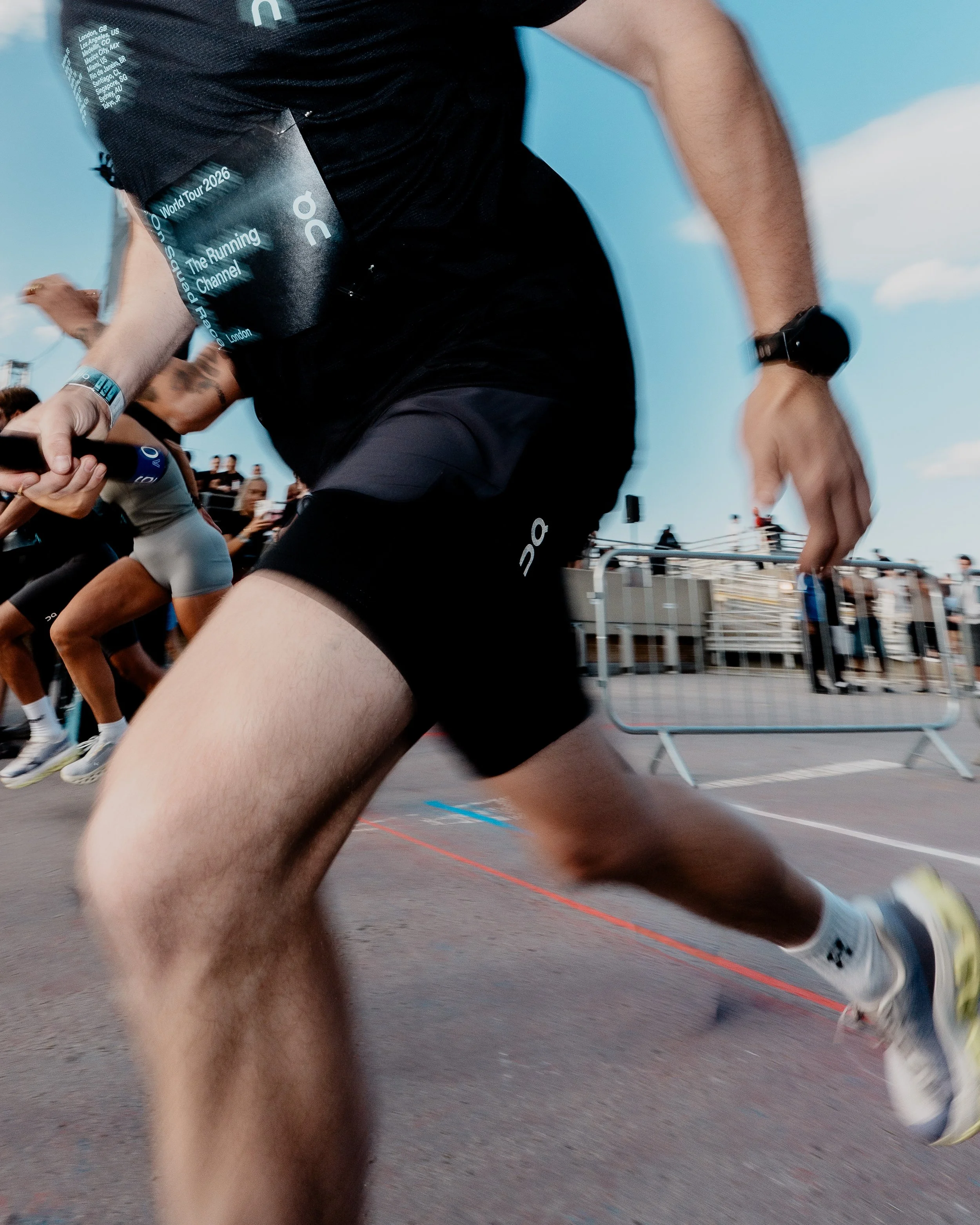 A person in athletic attire running outdoors during a race or event, with spectators in the background, under a blue sky with clouds.
