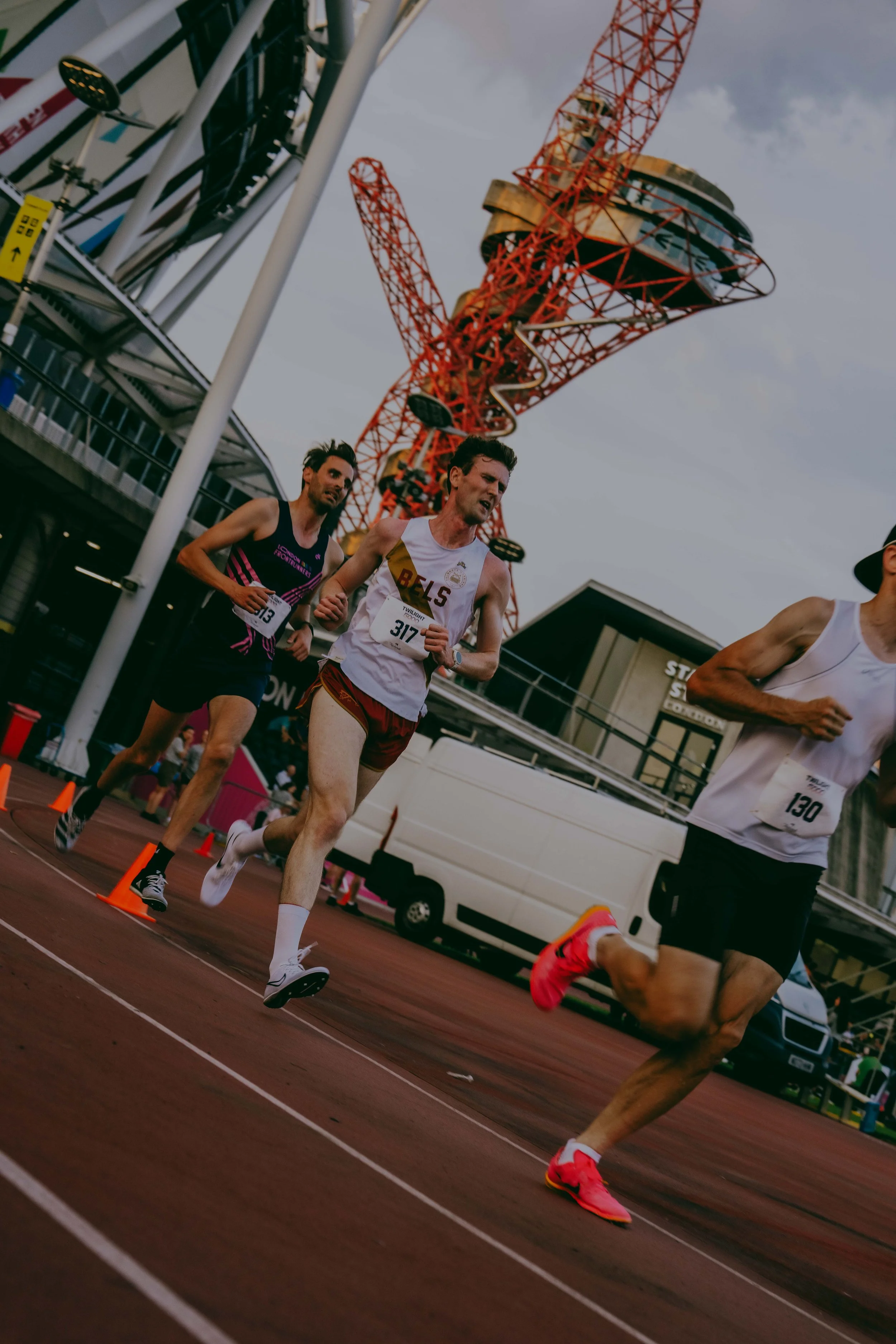 Group of runners competing in a track race, with a large red crane and a modern building in the background.