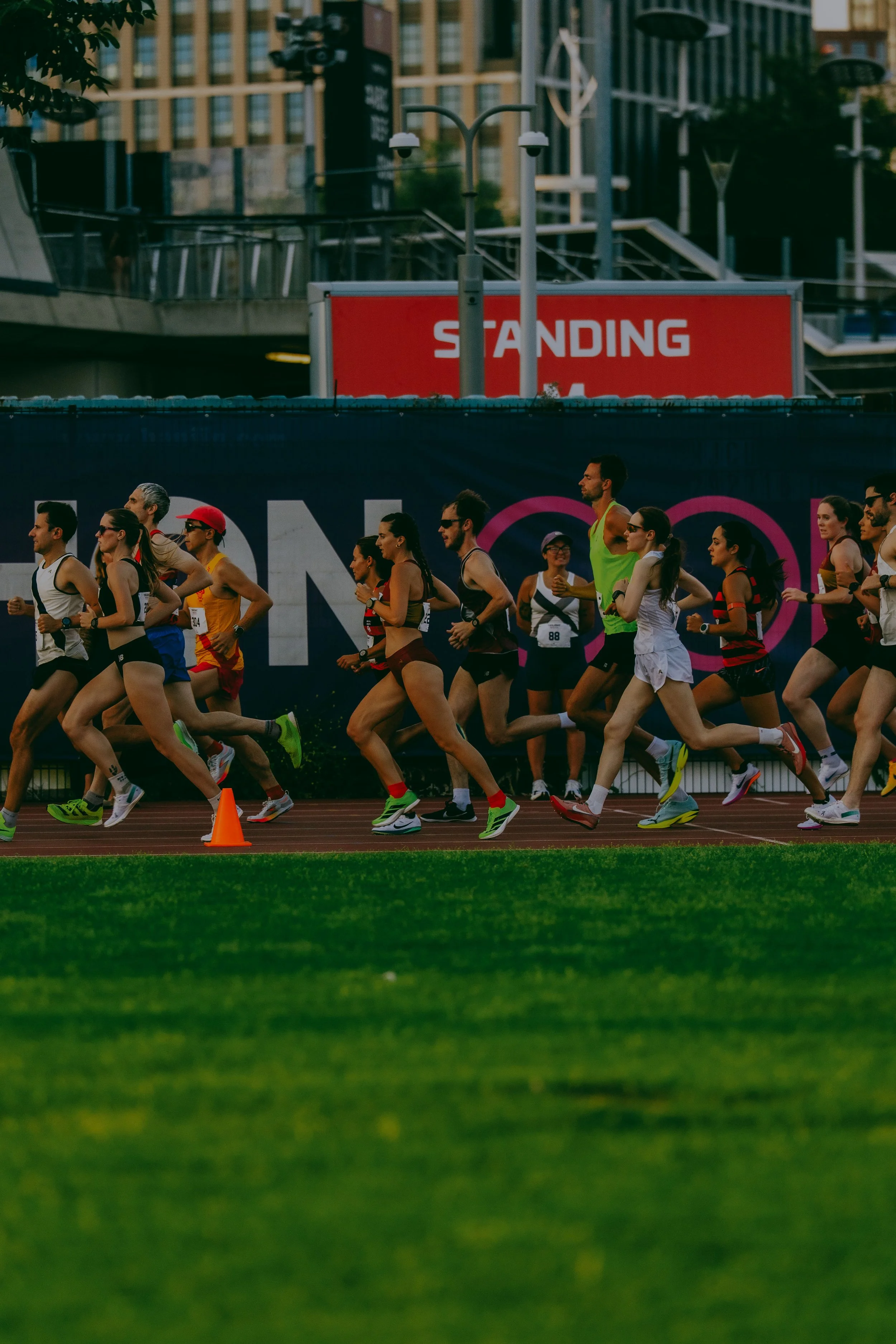 A group of runners participating in a race on a track, with a red and white sign that says 'STANDING' above them.