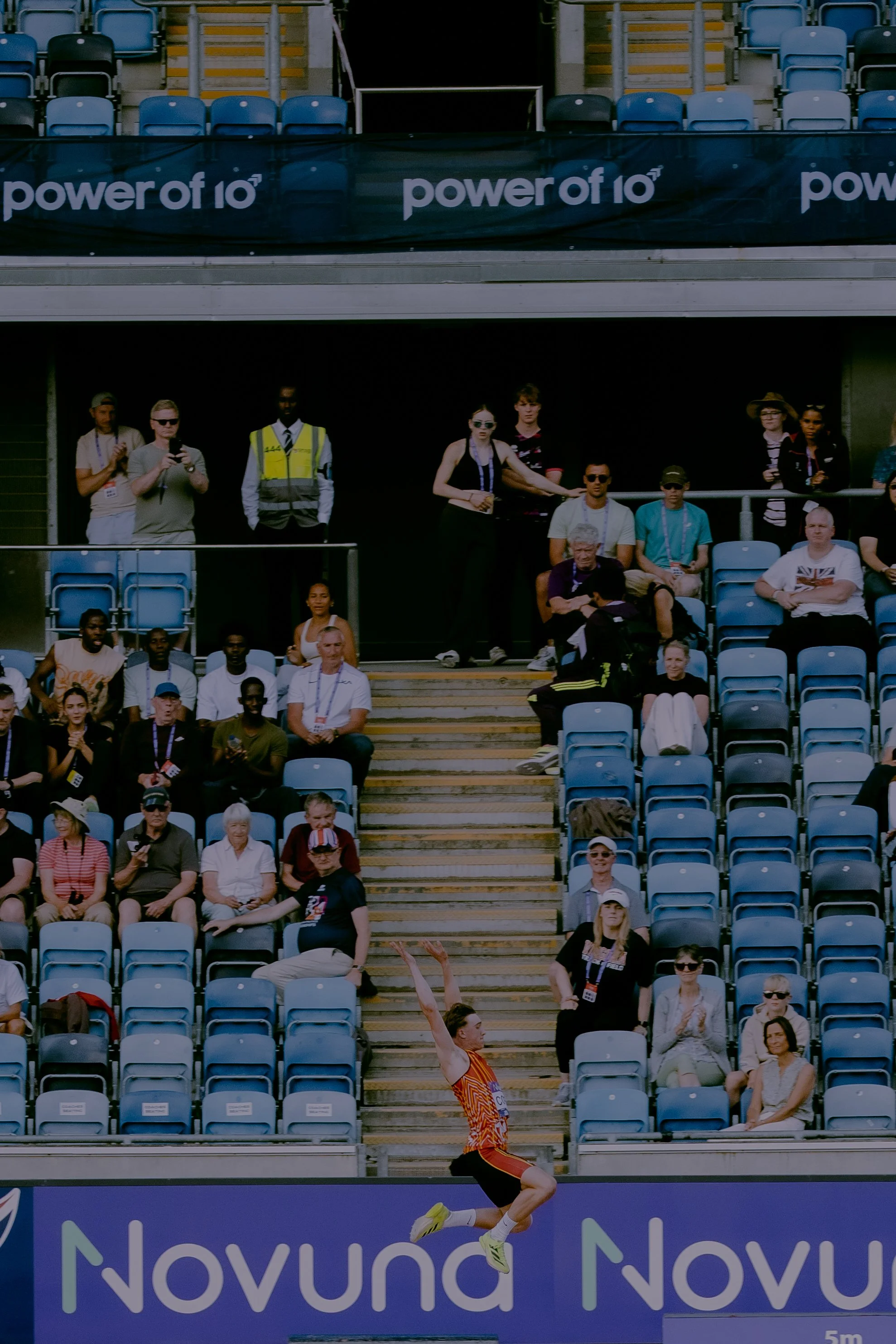 Athlete running on track during a competition with spectators in the stands watching.
