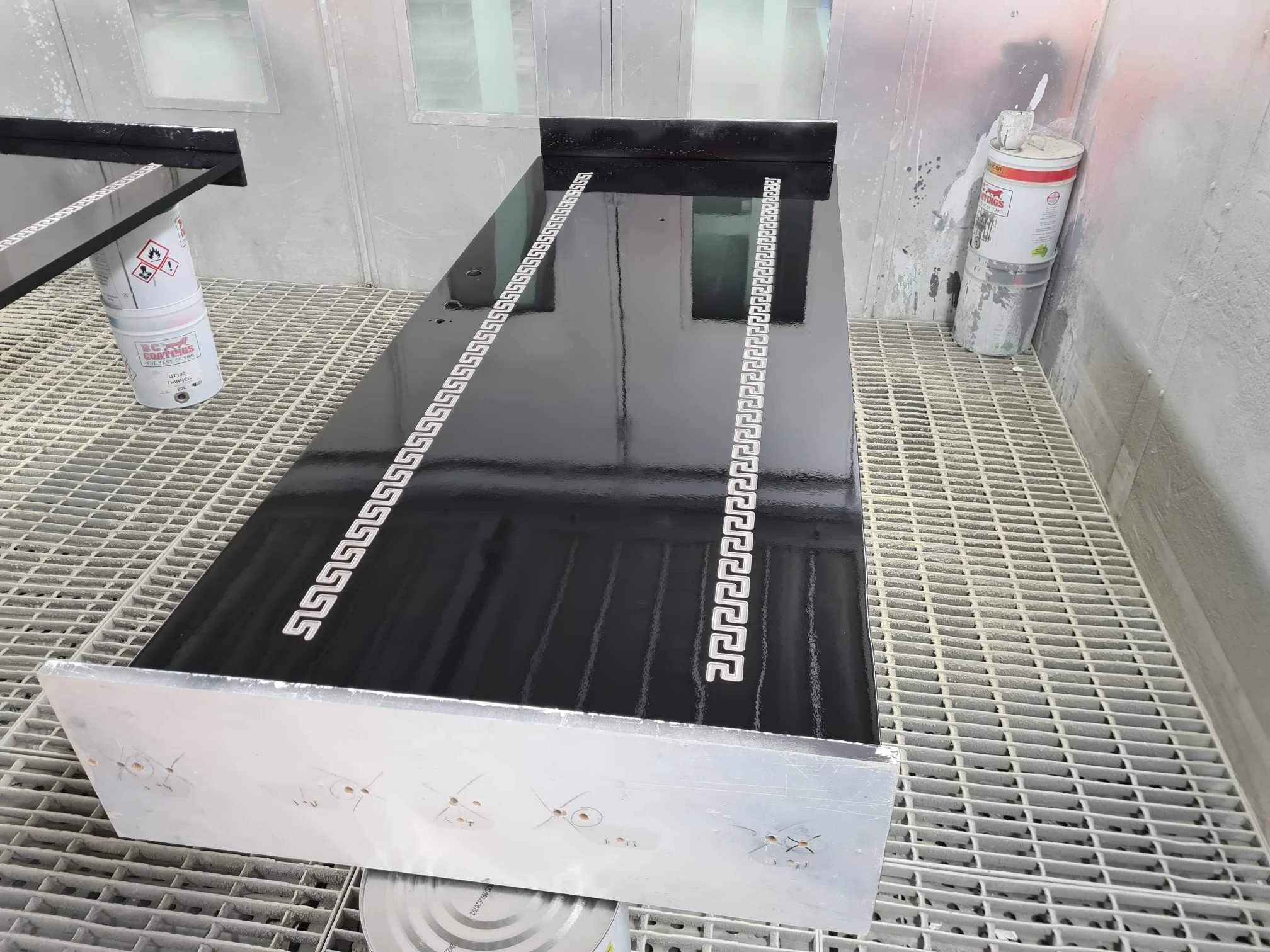 Black and white countertop with Greek key pattern inlaid along its length, placed on a white grated surface, with paint cans and equipment in the background.