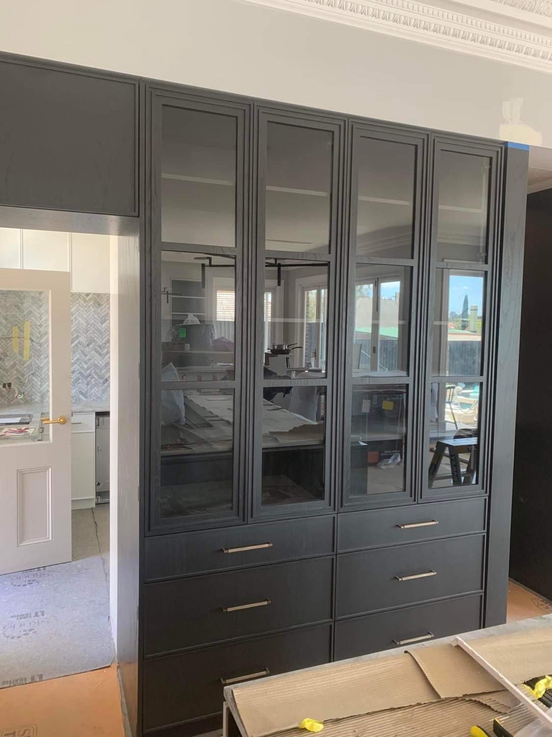 A black wood china cabinet with glass doors and drawers, partially assembled in a living room.