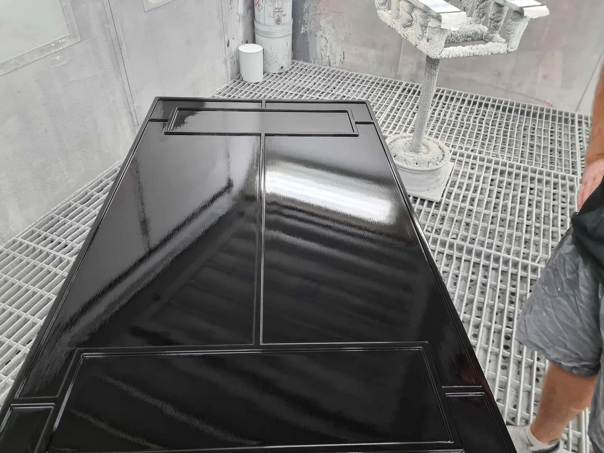 Black, glossy door panel in a spray booth with protective grates on the floor and equipment in the background.