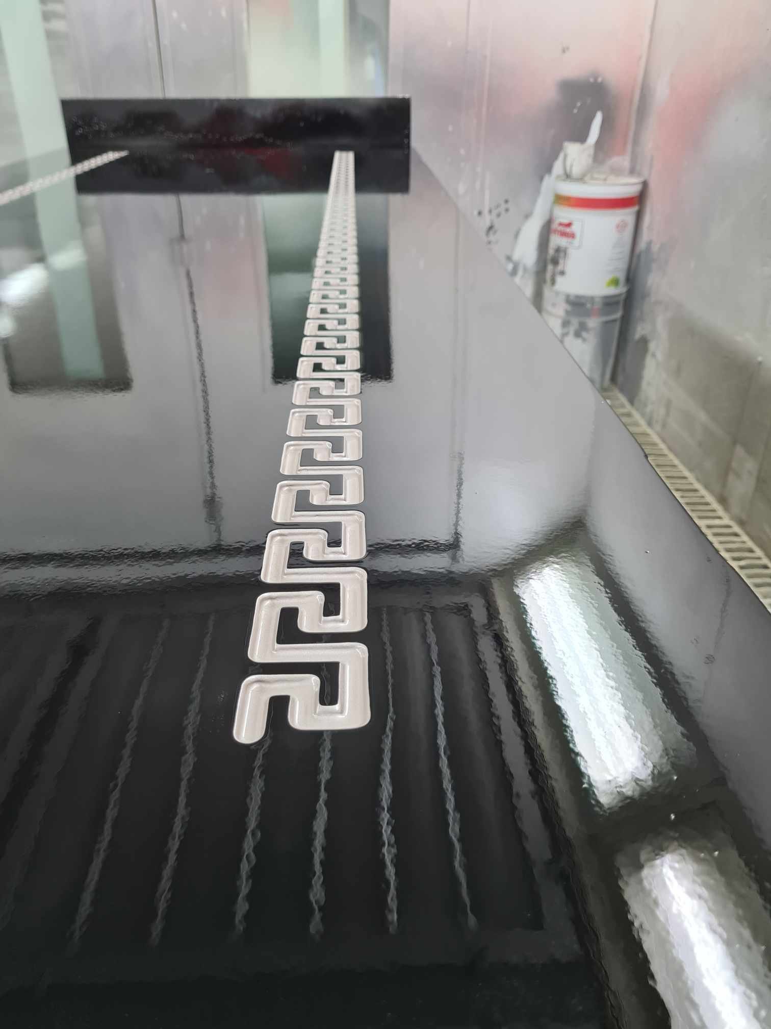 A black surface with a row of white Greek key pattern spacers running along its length, in a workshop or industrial setting.