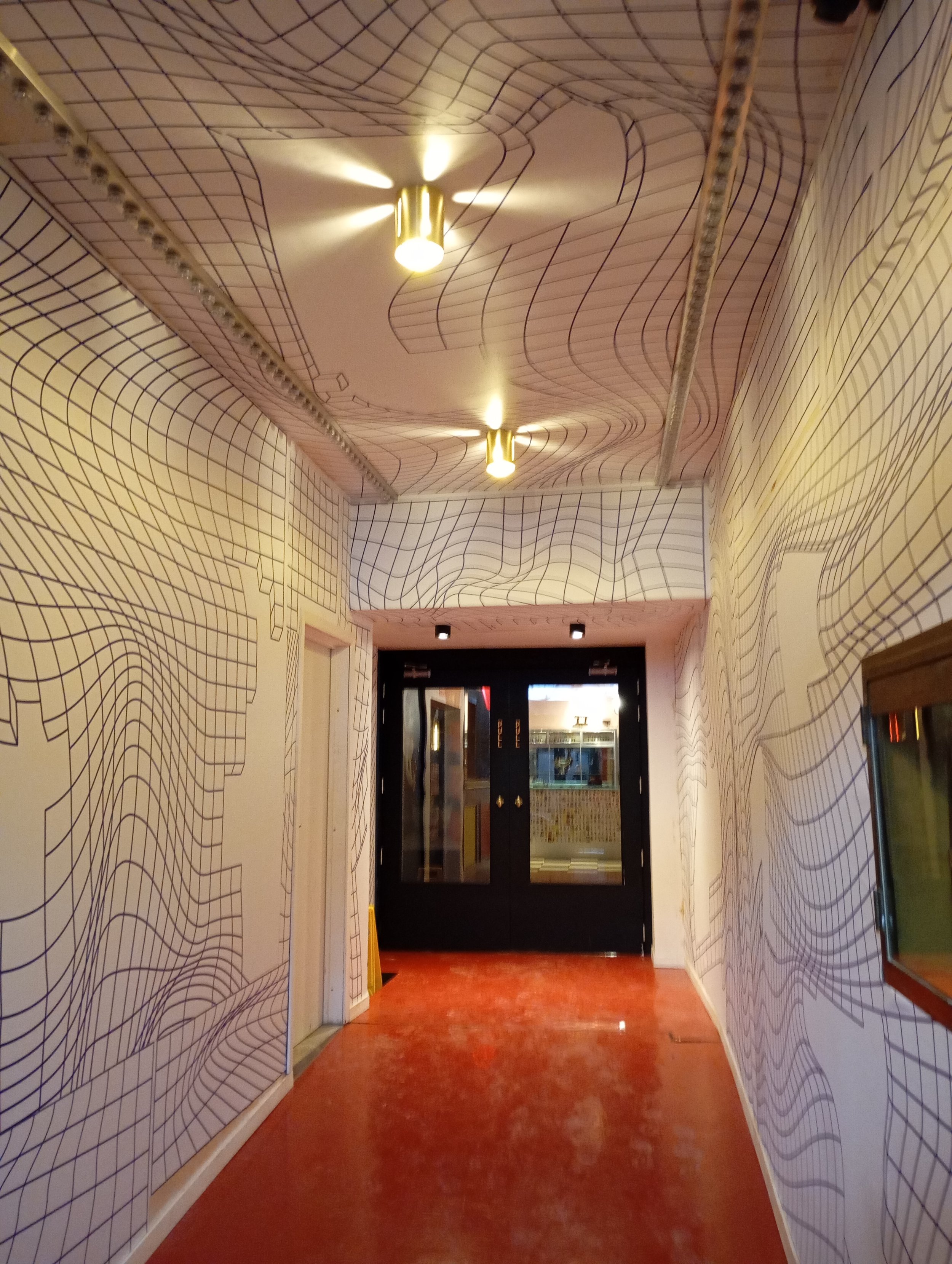 Couloir intérieur décoré avec un mur et un plafond recouverts d'une création de l'artiste J.Demski , art art mural abstrait en lignes noires entremêlées géométriques. Deux plafonniers lumineux et des fenêtres à droite.