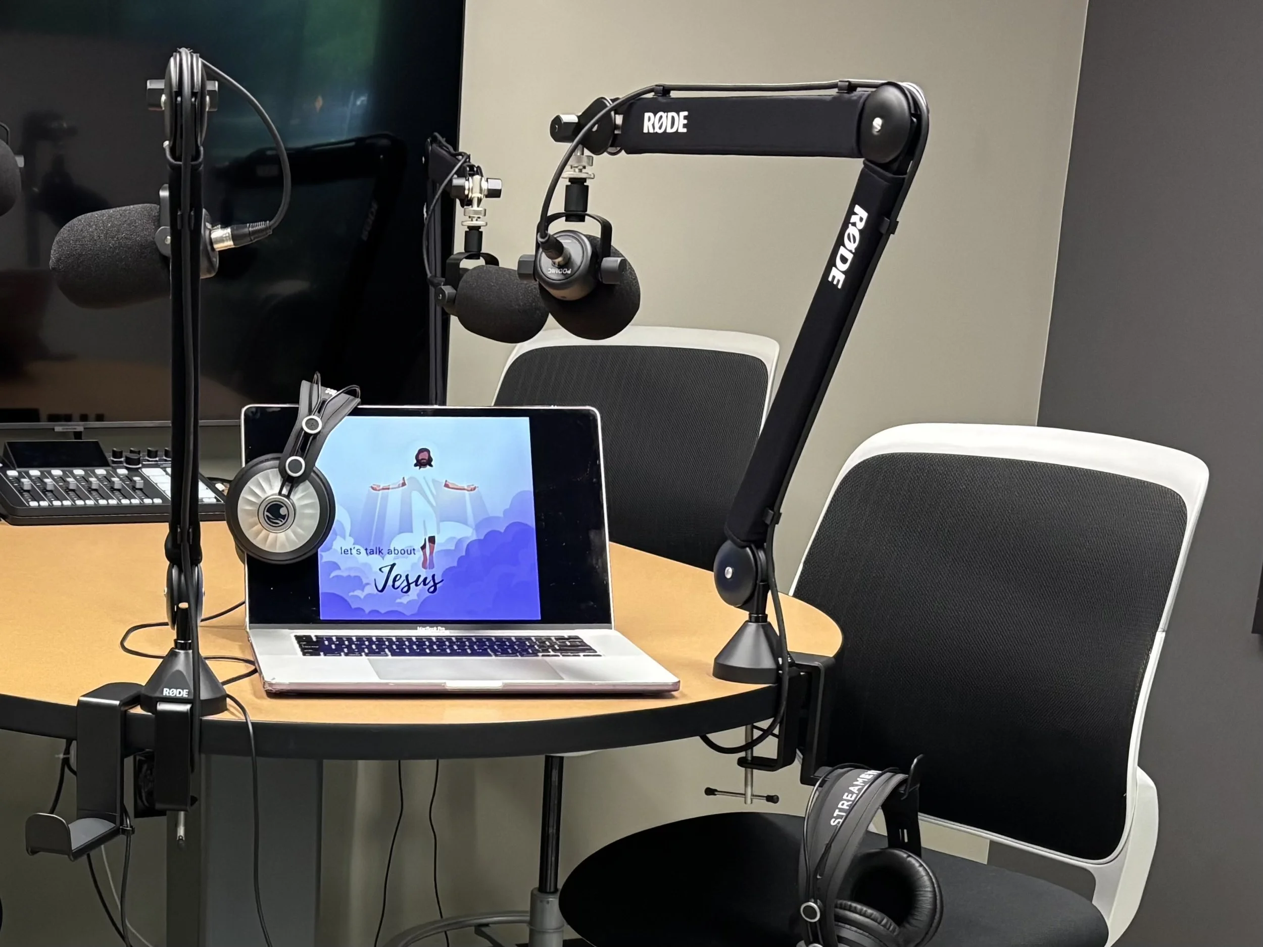Recording studio setup with microphones, headphones, a laptop displaying Christian imagery and text, and chairs.