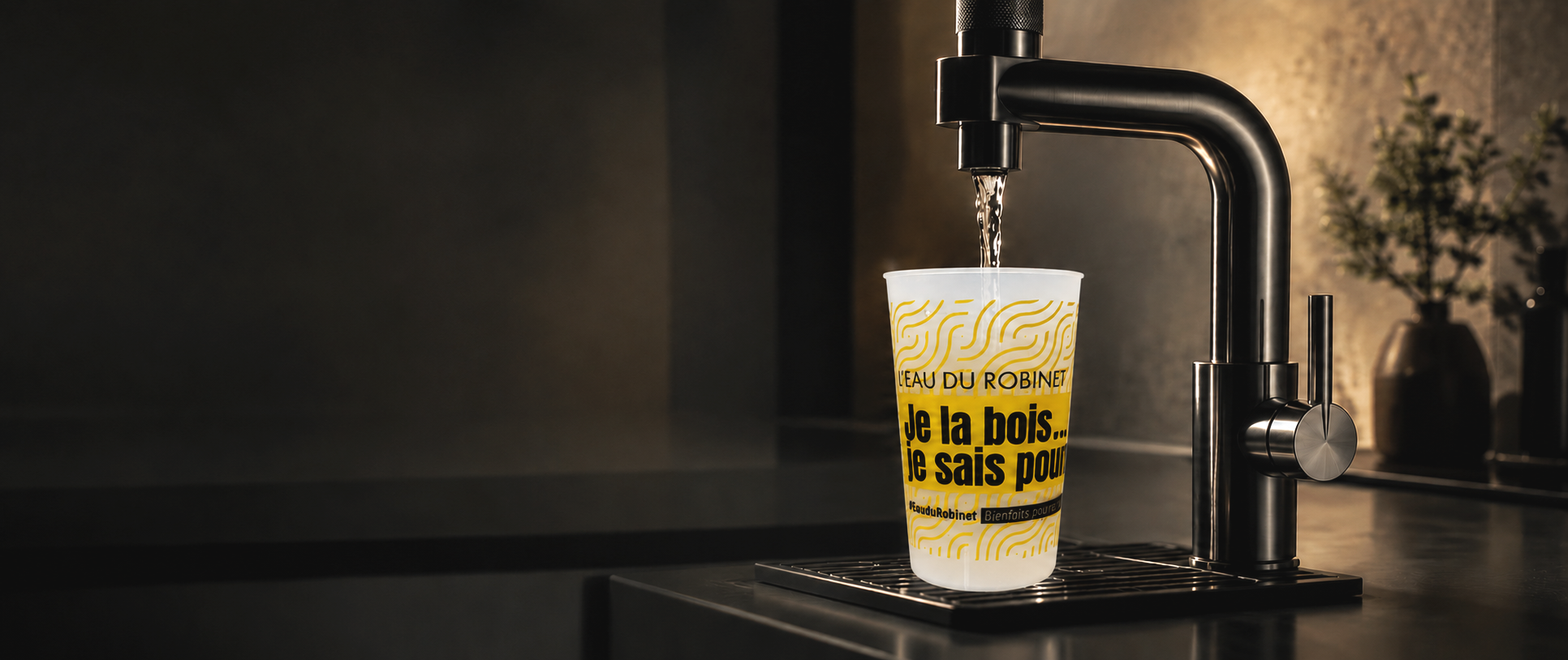 Verre en plastique blanc avec inscription en français, sous un robinet d'eau, dans une cuisine moderne.