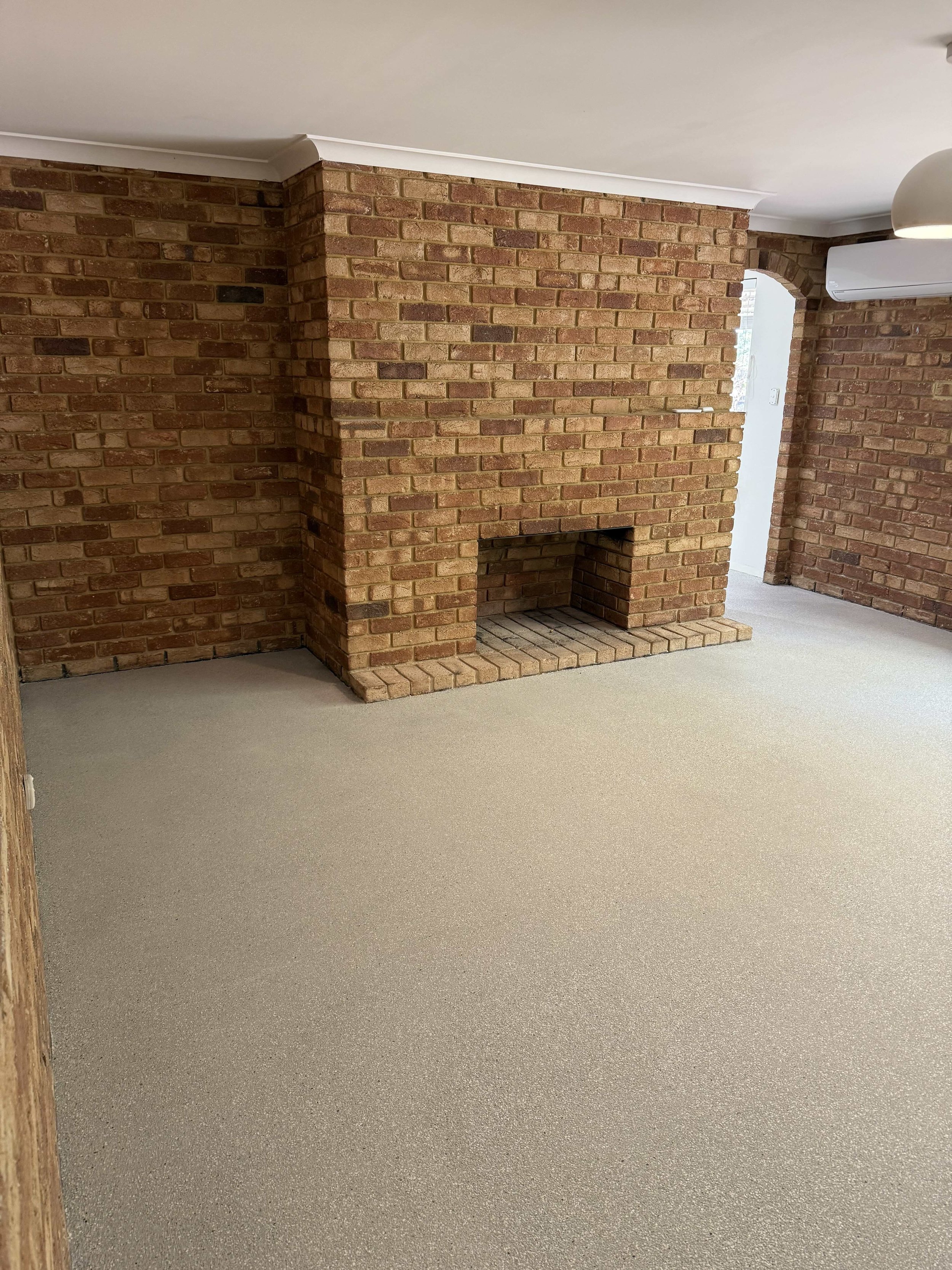 Epoxy flake Perth in a Room with red brick walls, a brick fireplace, beige carpet, and white ceiling molding.