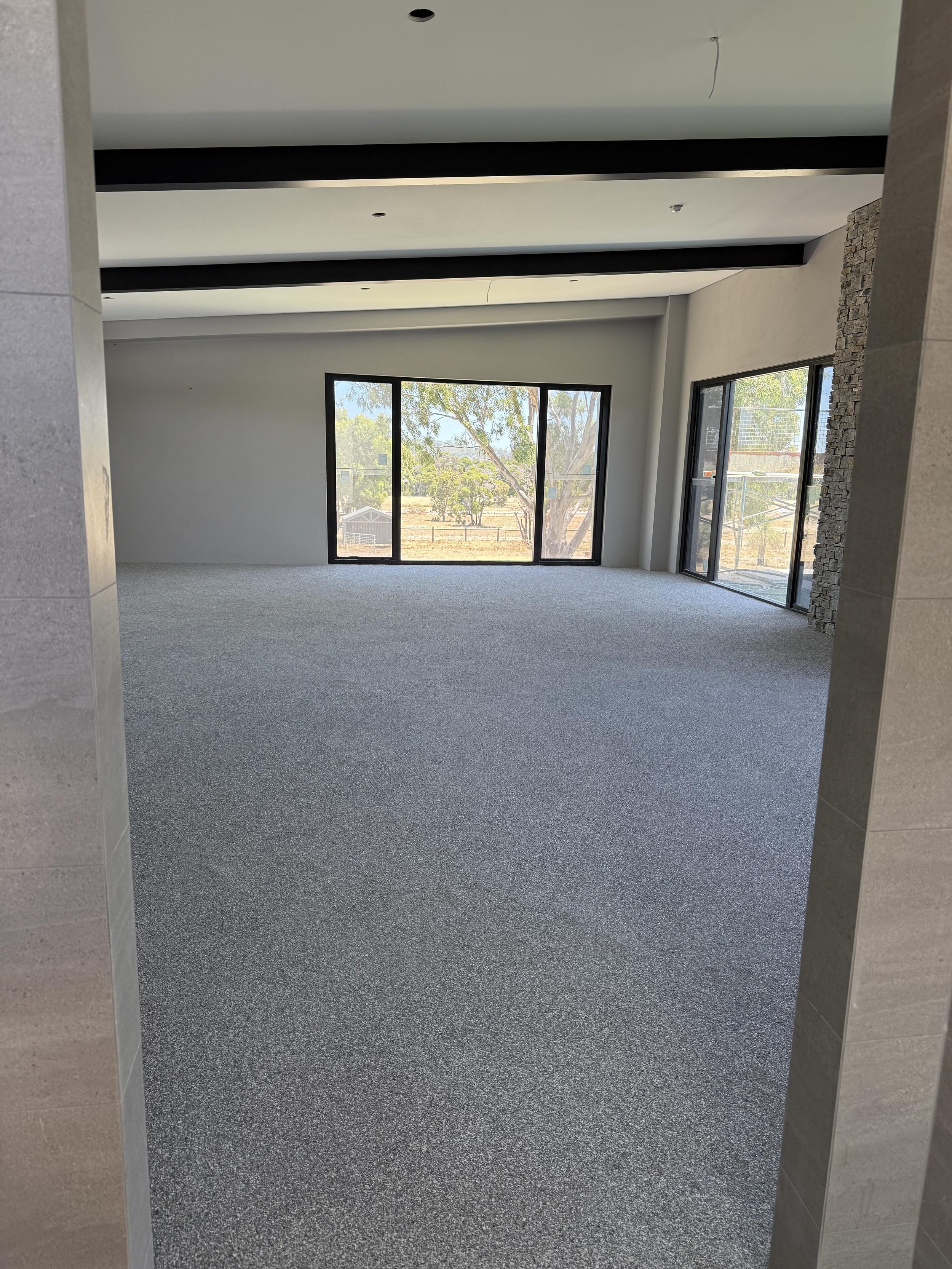 Epoxy flake Perth room with large windows and sliding glass doors, gray carpeted floor, and partial wall with stone exterior finish.