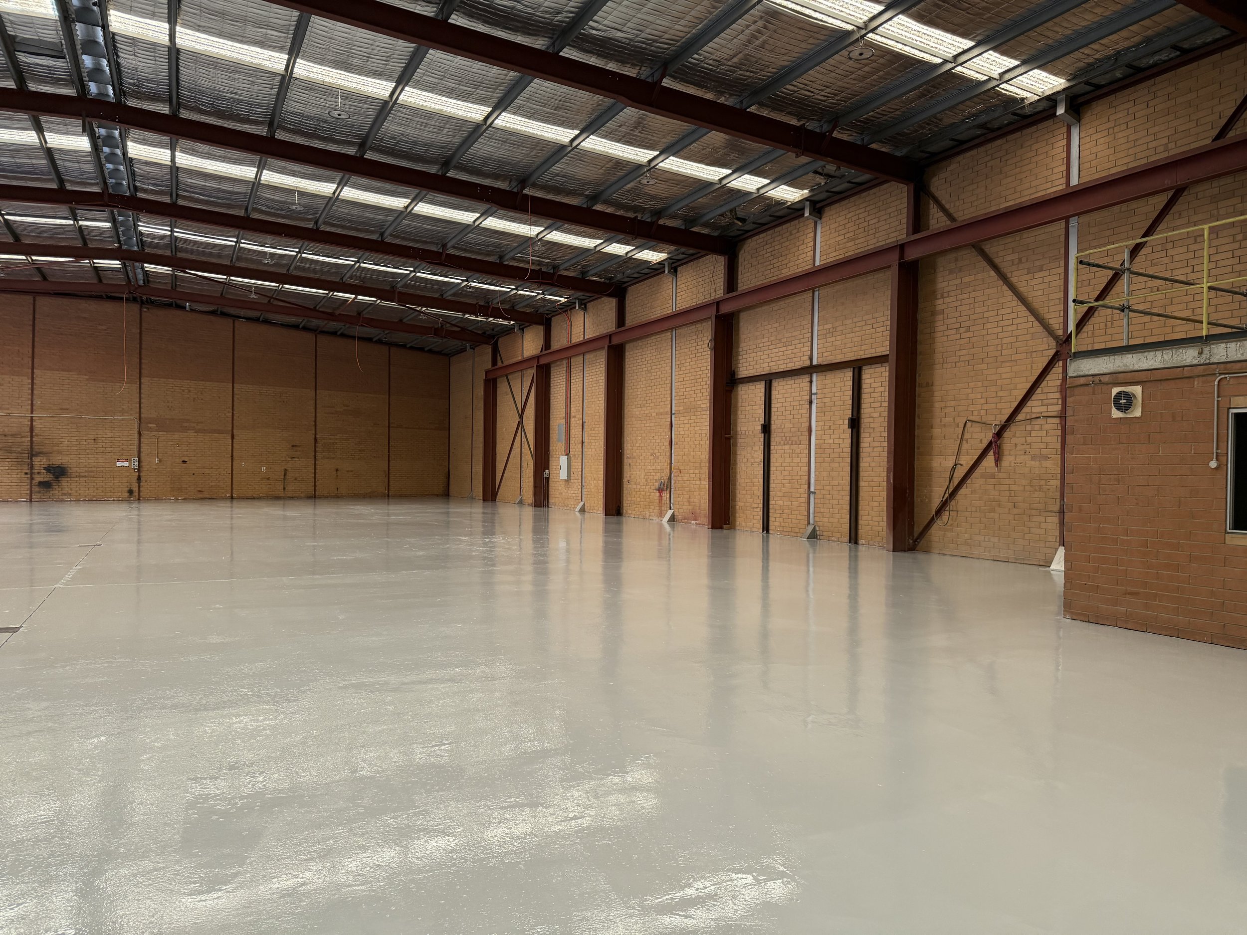 Epoxy flooring in Perth warehouse with brick walls, a high metal roof with skylights, and a polished concrete floor.