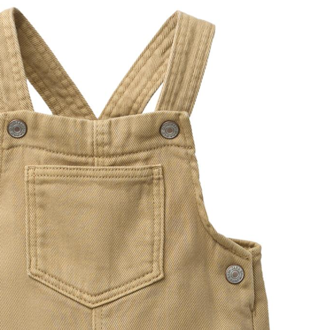 Close-up of a pair of tan overalls with a front pocket and metal buttons.