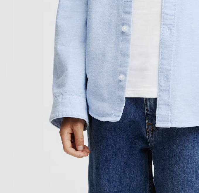 Close-up of a person wearing a light blue denim shirt over a white T-shirt and dark blue jeans.