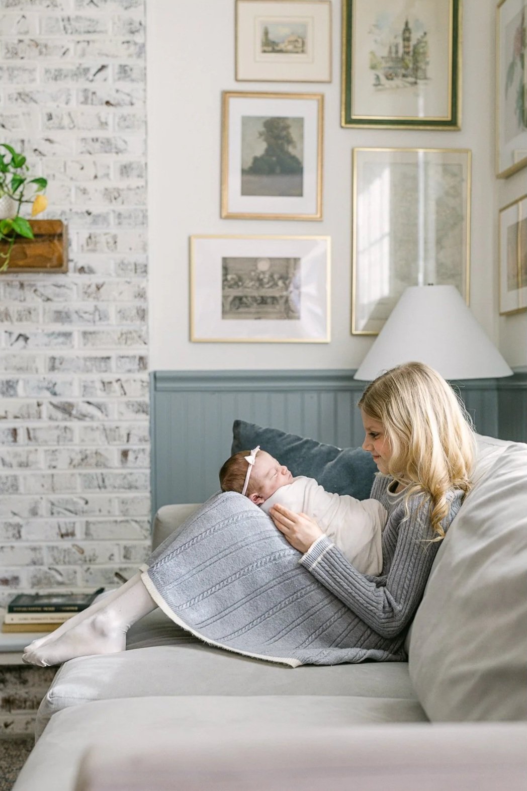 baby girl swaddled and being held by her big sister on the couch with a wall art gallery designed by Aberle Design Co. in the backdrop