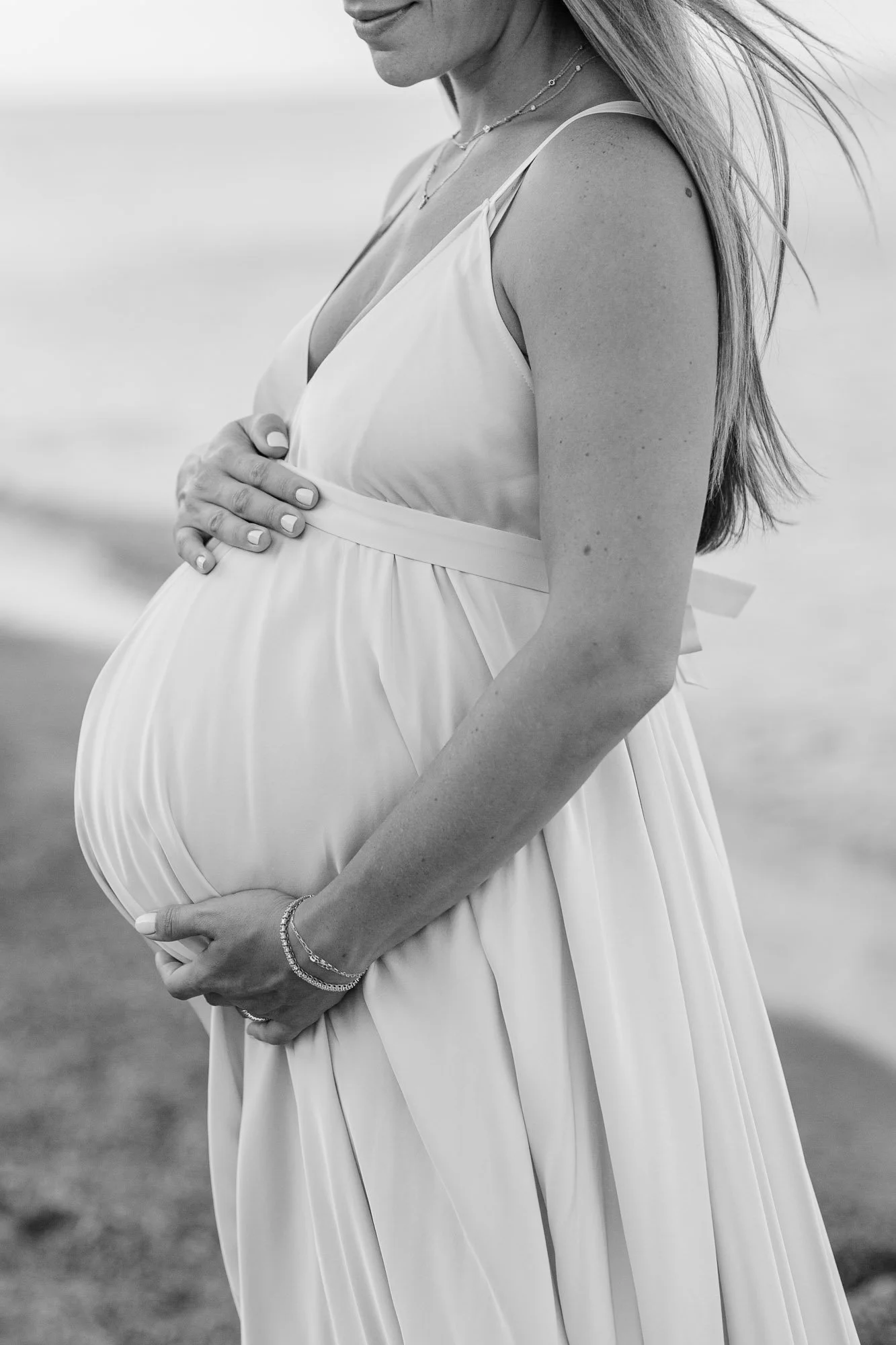 closeup black and white edit of a pregnant mom holding her baby bump while standing on Glencoe Beach during a maternity session