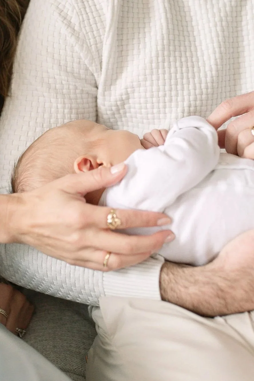 close up image of a newborn baby being cradled by her dad with her mom's hand also embracing her