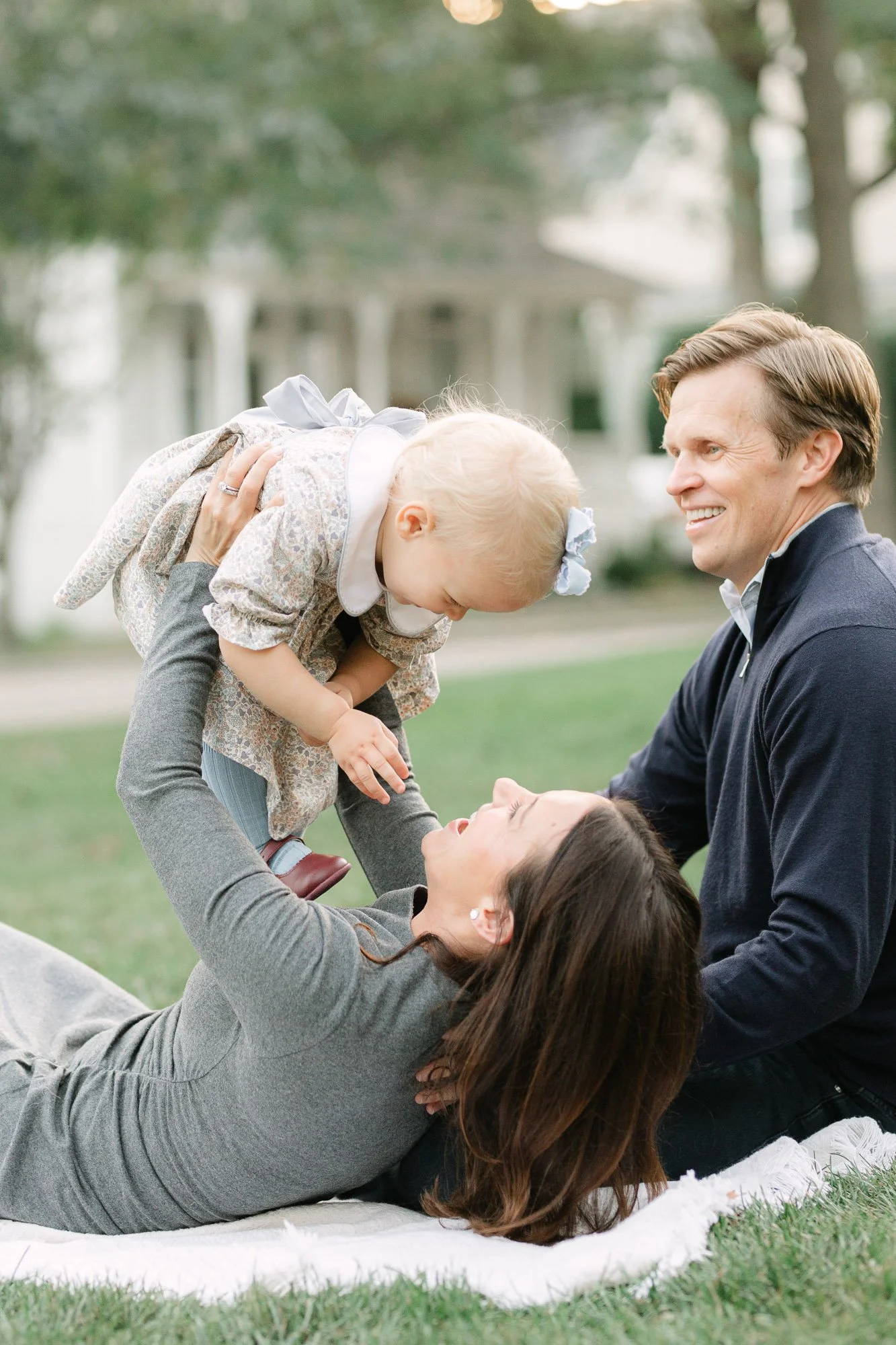 mom holding her toddler daughter over her head with dad smiling next to her during a first birthday family session in arlington heights