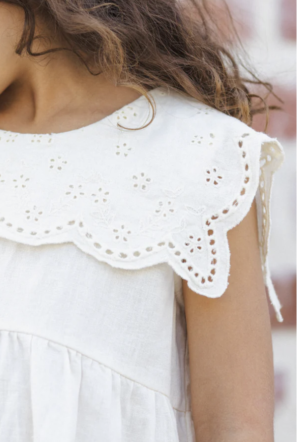 Close-up of a white dress with eyelet embroidery on the sleeves and collar, and a slightly gathered bodice.