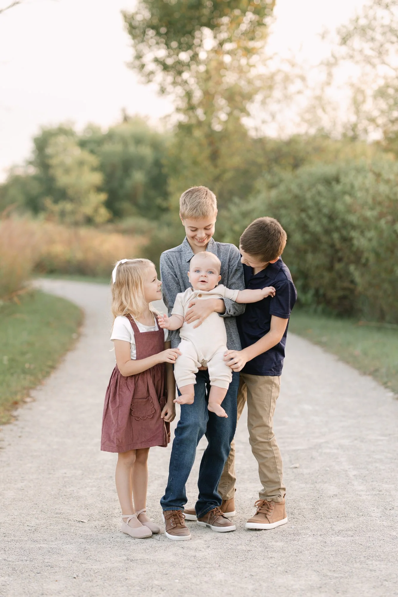 family of 4 siblings smiling at their baby brother during an outdoor family session in Long Grove