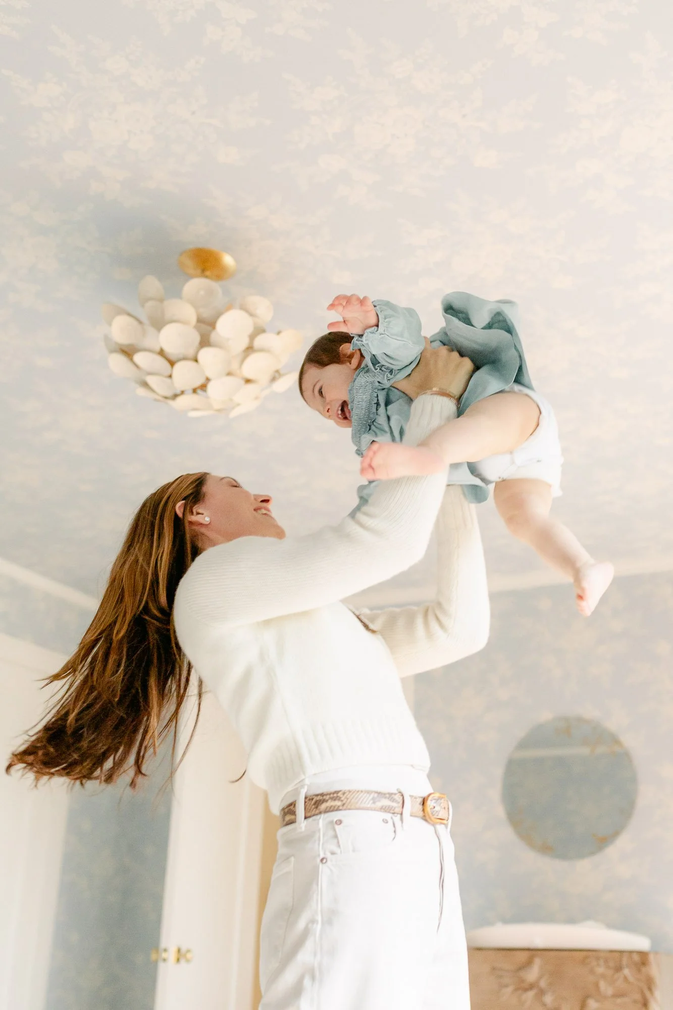 mom picking up her toddler daughter to swing her around during a lifestyle home family session in Glencoe Beach