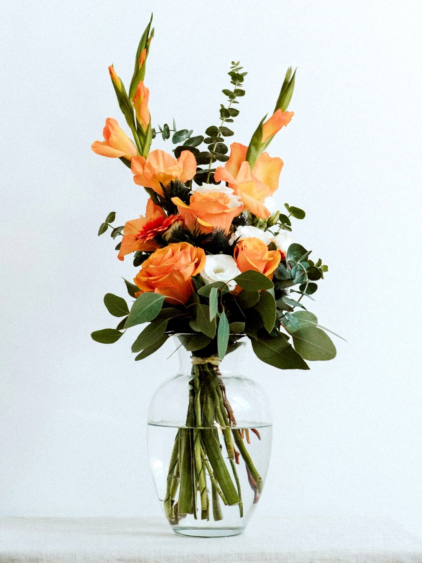 A bouquet of orange and white flowers in a clear glass vase with water.