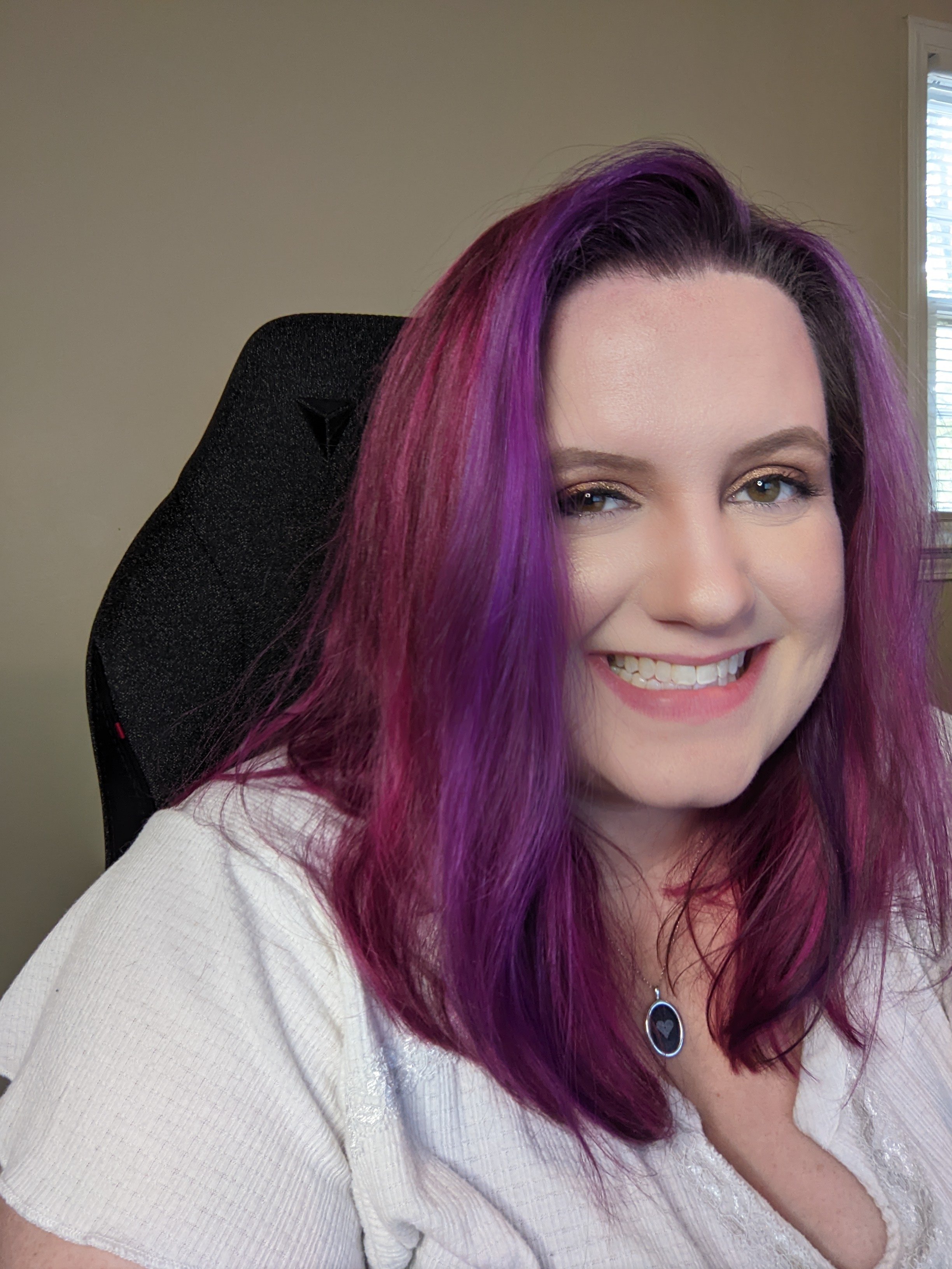 Desiree, smiling in a desk chair. She has pink and purple hair and a white shirt.