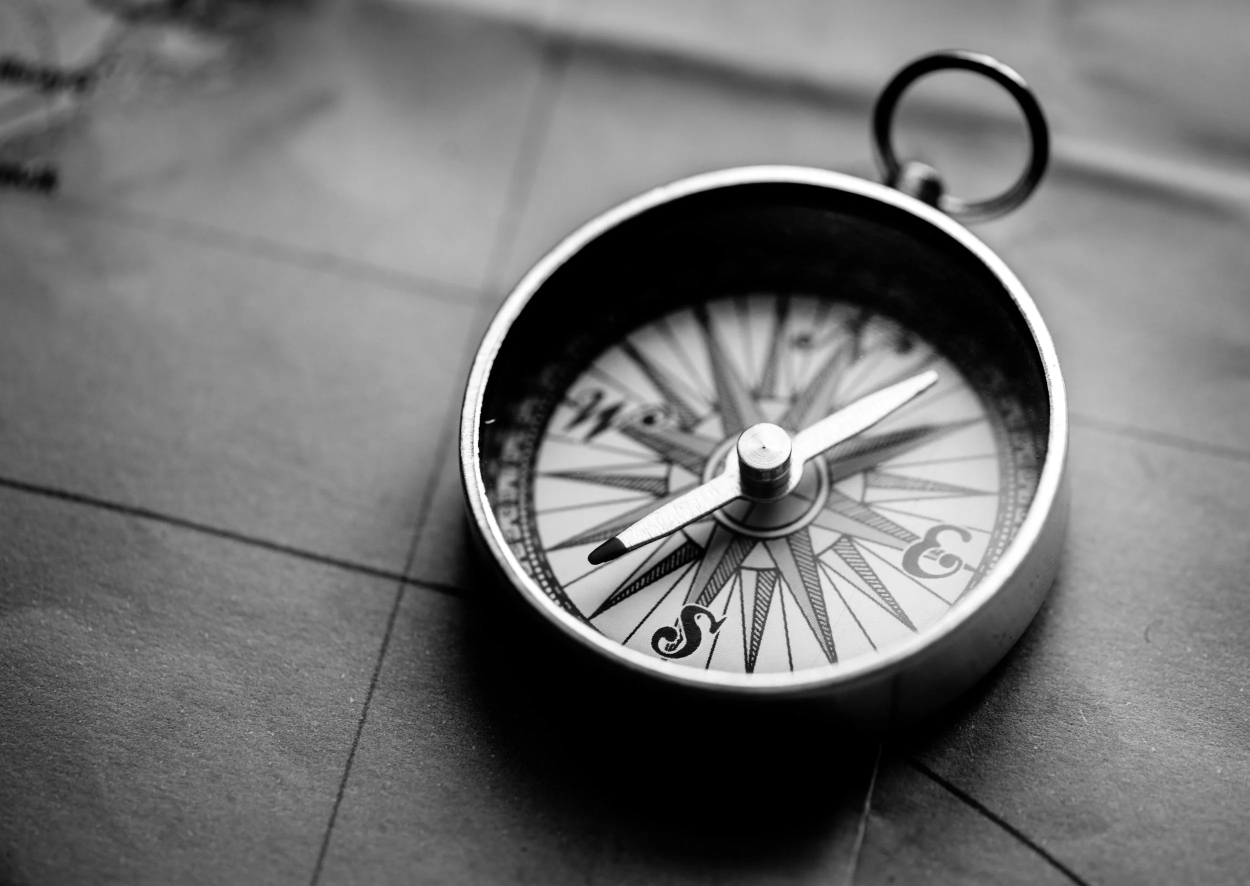 A black and white photograph of a compass on a wooden surface, showing the needle pointing northeast.
