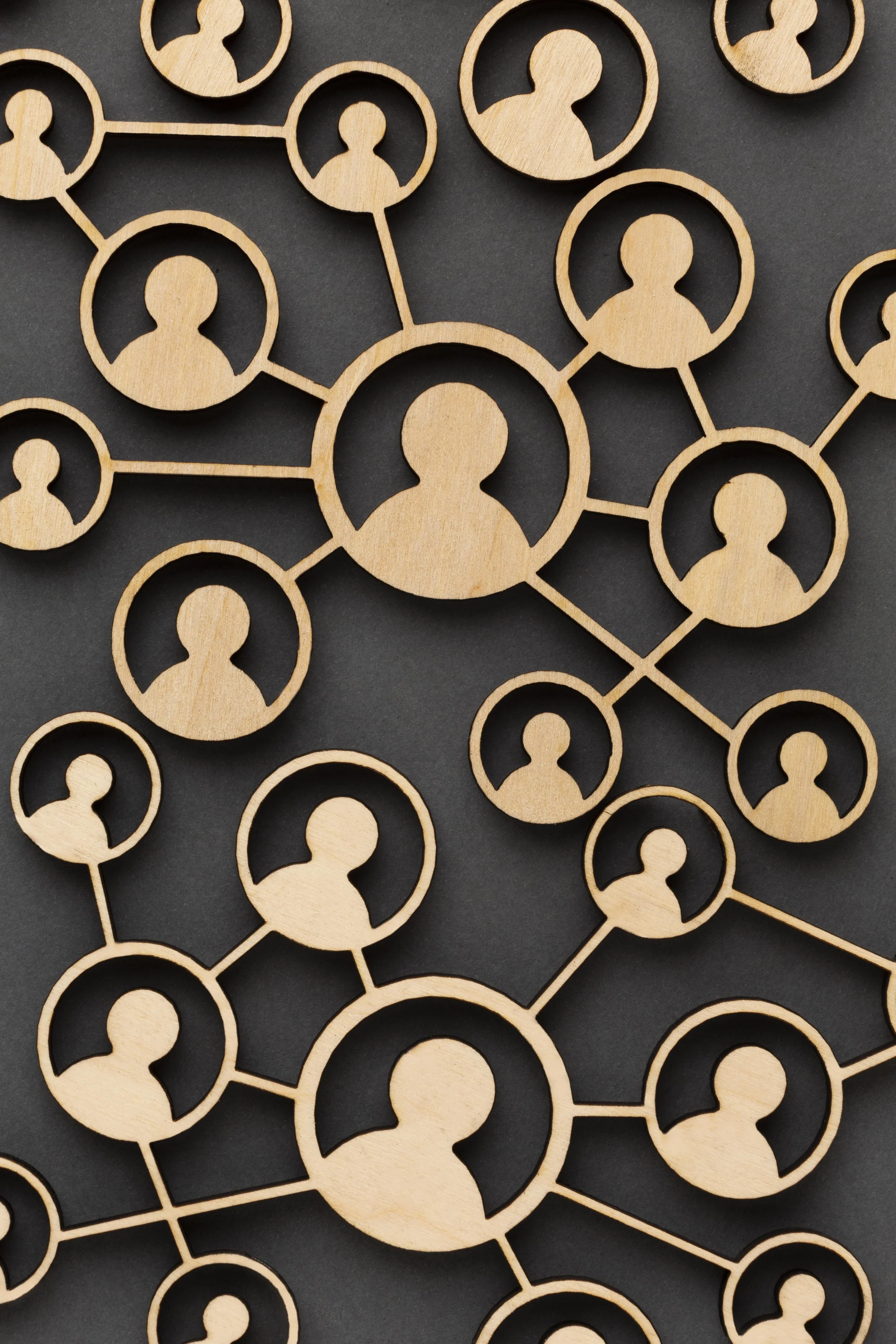 Wooden cutout representing a network of interconnected human figures on a dark background.