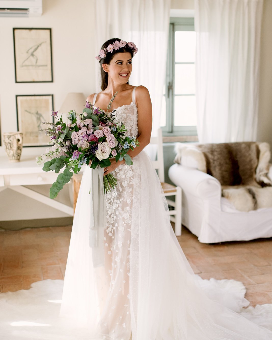 A quiet moment before the vows &mdash; our radiant bride, glowing with joy, holding a bouquet of clematis, roses, lavender, and eucalyptus, framed by the soft Tuscan light in her room at Conti di San Bonifacio. Wearing a couture gown by Dutch designe