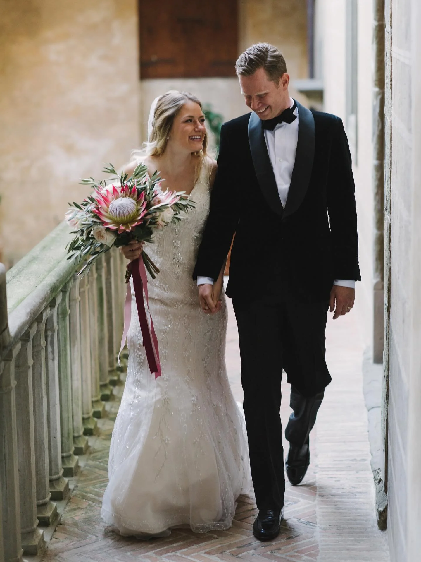 A just-married walk at Castello di Montegufoni, holding a bouquet that feels as bold as the moment itself.

A statement king protea at the center, surrounded by soft roses and textured greenery, finished with long silk ribbons that move with every st