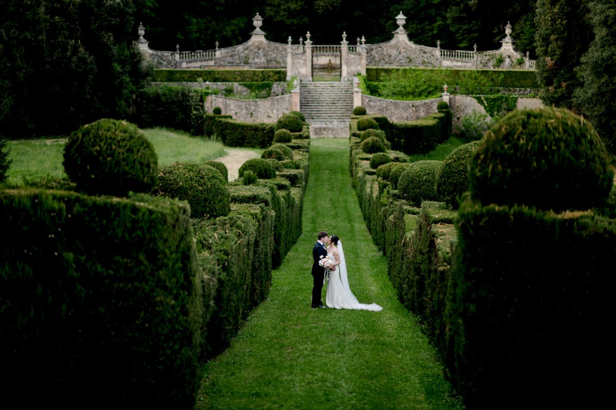 Bruidspaar kust elkaar in een Italiaanse tuin tijdens hun bruiloft bij Castello di Celsa – een romantisch moment van trouwen in Toscane, vastgelegd door FunkyBird: Tuscany wedding photographer en bruidsfotograaf in Italië.